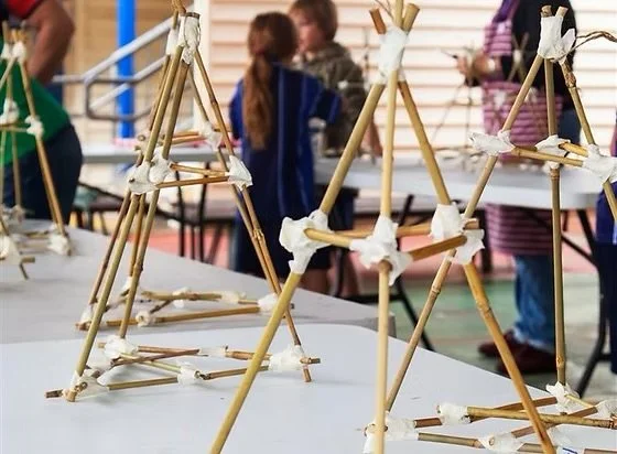 Several small structures made from sticks, with people in the background.