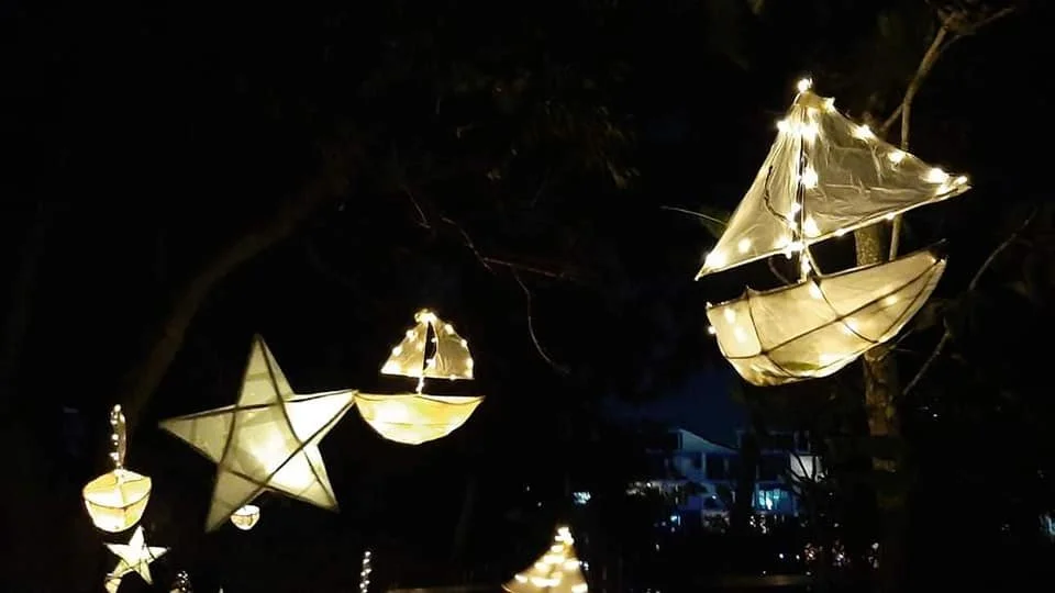 Decorative paper lanterns shaped like stars, boats, and other objects hanging from tree branches at night.