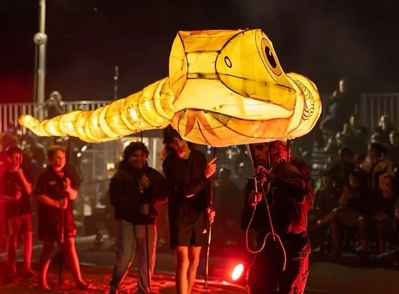 People holding a large, illuminated snake-shaped lantern puppet during a night festival or parade.