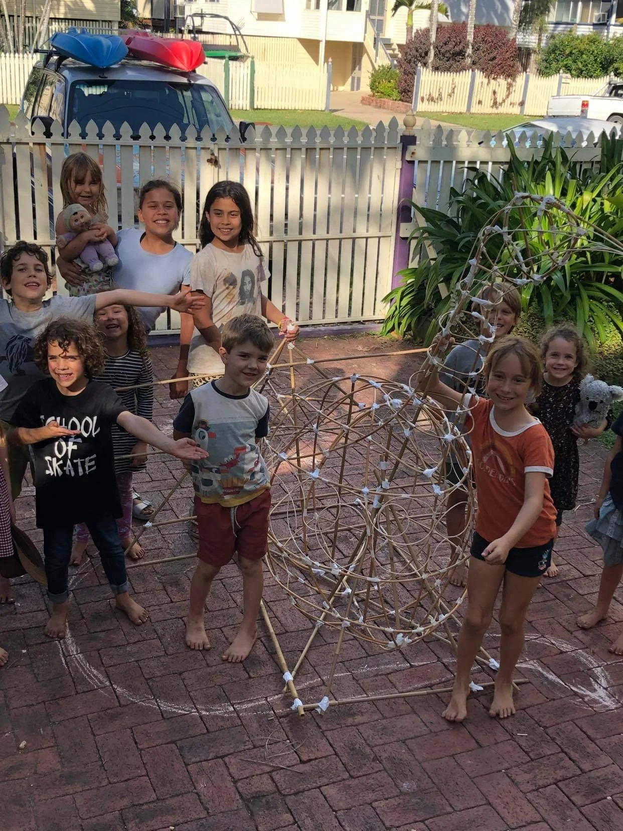 Group of children in a workshop outside with a large lantern frame, some holding it and others smiling at the camera.