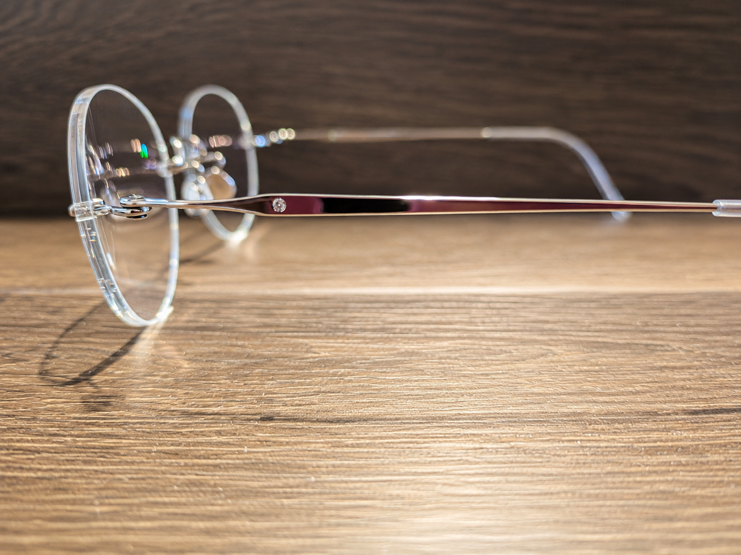 A pair of clear round glasses with silver temples resting on a wooden surface.