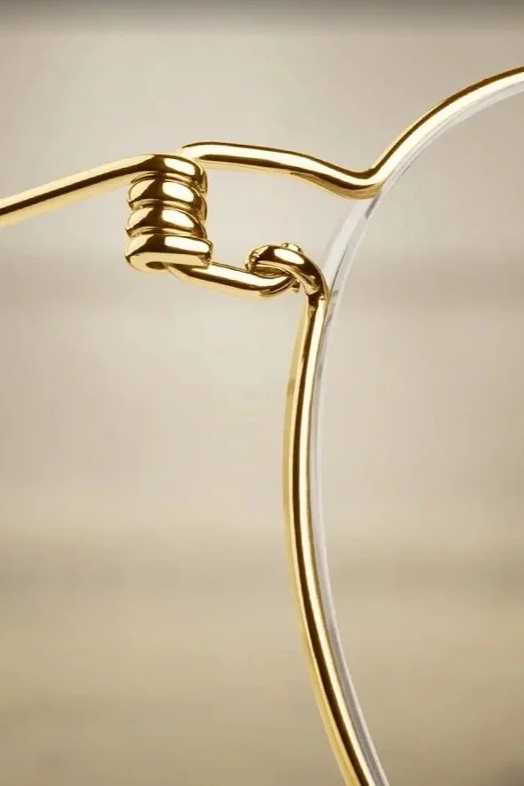 Close-up of a gold wire sculpture resembling a spoon and a fork, interconnected in a minimalist design.