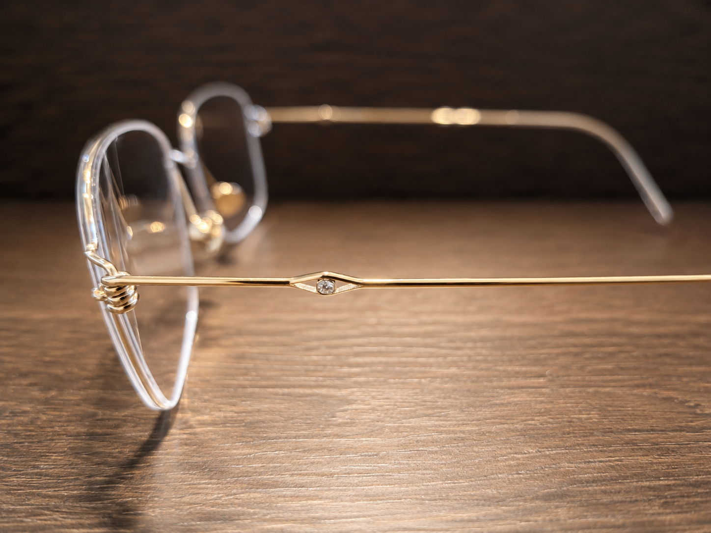 A pair of glasses with gold frames and clear lenses resting on a wooden surface.