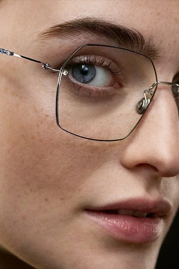Close-up of a person wearing square-framed glasses, showing blue eye, eyebrow, and part of nose and lips.