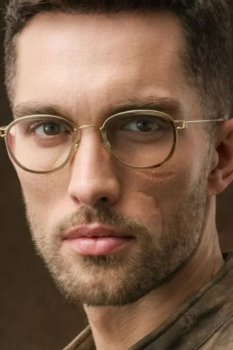 Close-up of young man with glasses, short hair, and light beard, looking directly at the camera.