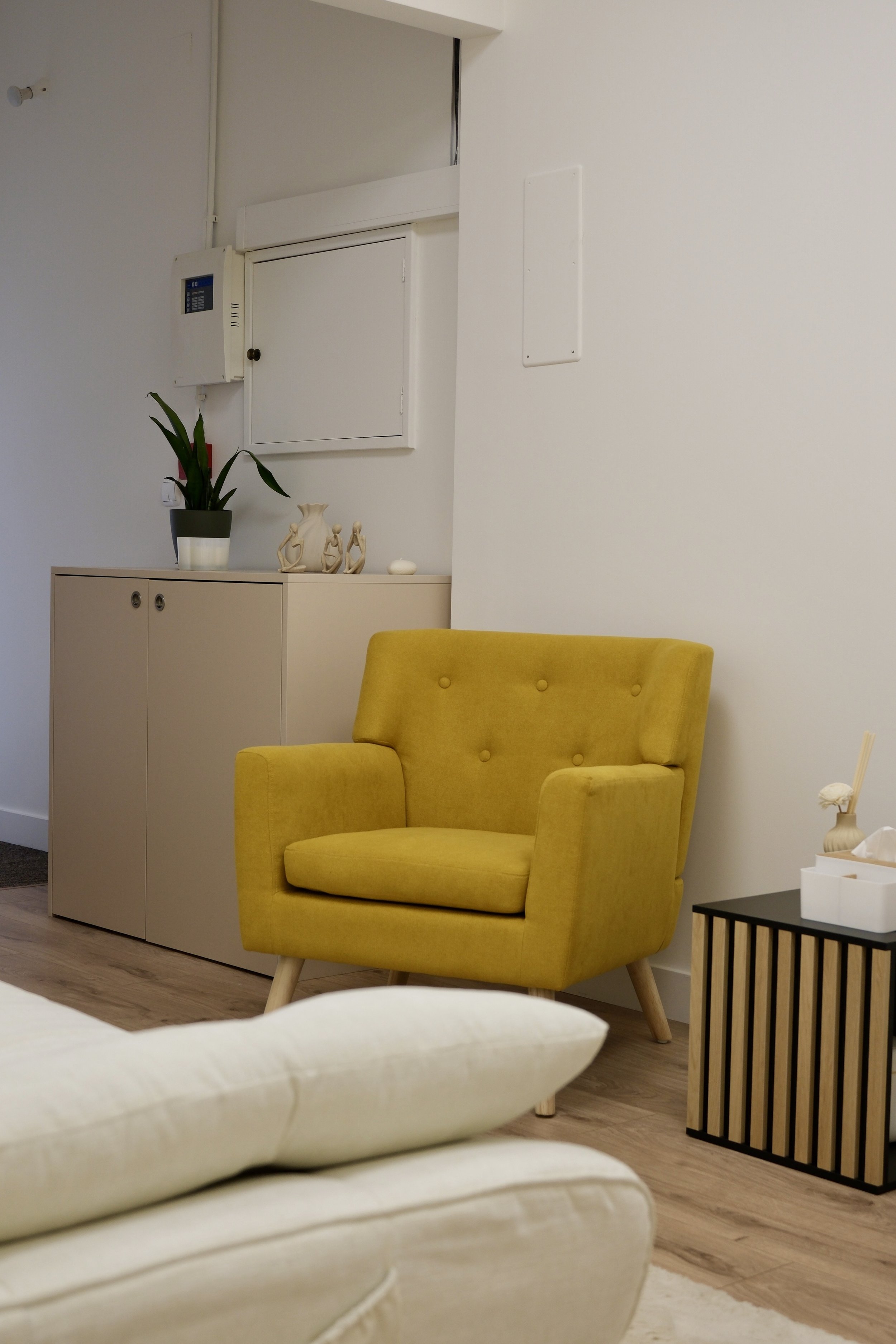 Consultório da Clínica Alma com poltrona amarela, mesa lateral preta, planta em vaso, objetos decorativos na parede, e mobiliário minimalista.