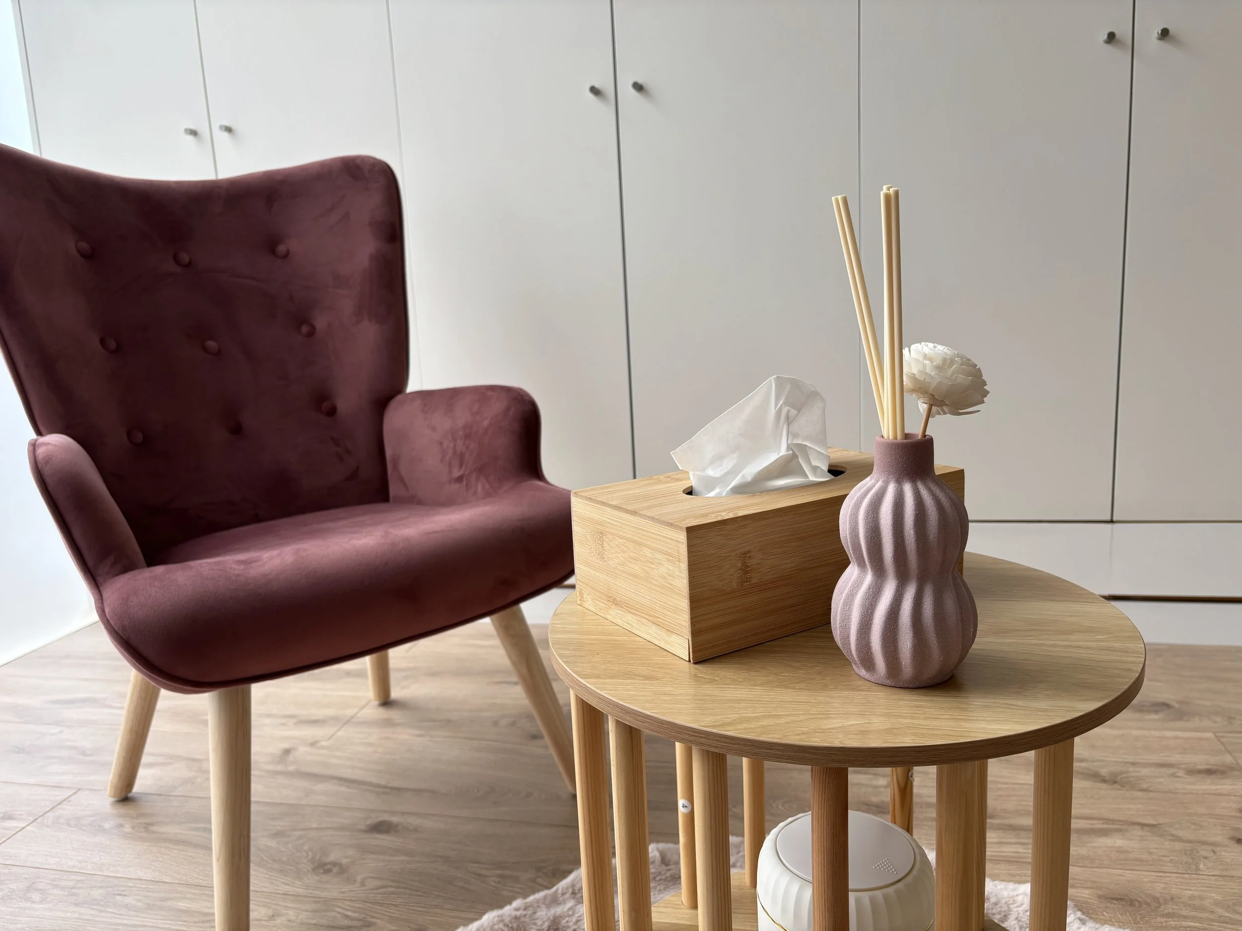 Consultório da Clínica Alma com um sofá de veludo roxo ao lado de uma mesa de madeira clara e um vaso roxo de cheiro.