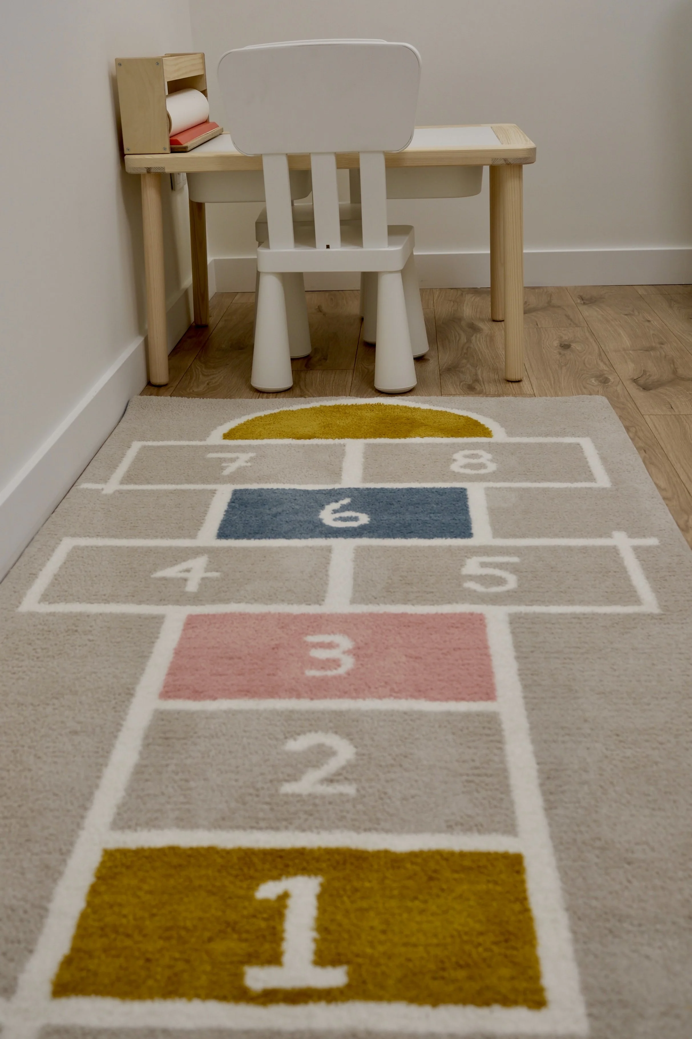 Tapete colorido do consultório da Clínica Alma, com números e cores. Ao fundo, uma mesa de madeira com uma cadeira branca diante de uma parede branca e piso de madeira.