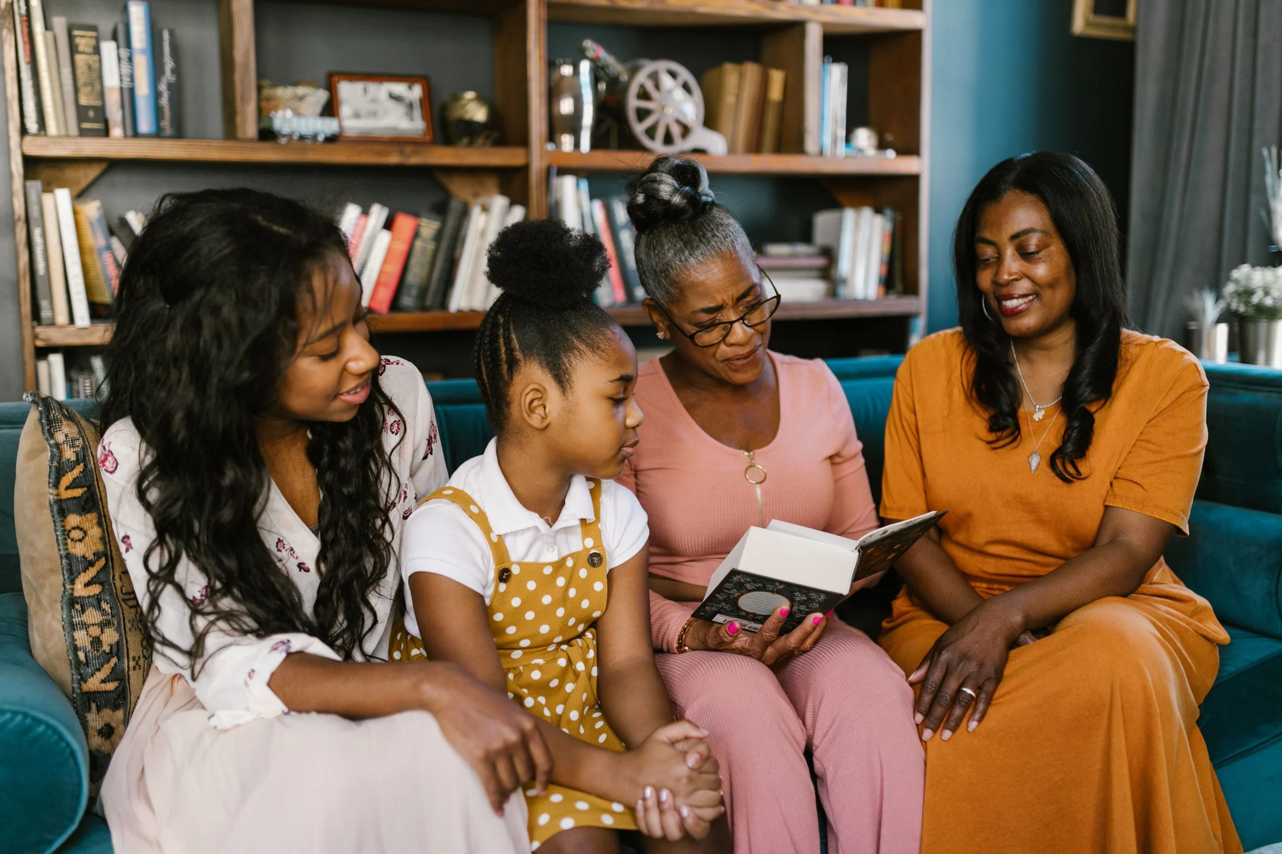 Three generations of a Black family reading a book together on a sofa, an elder reading to a child