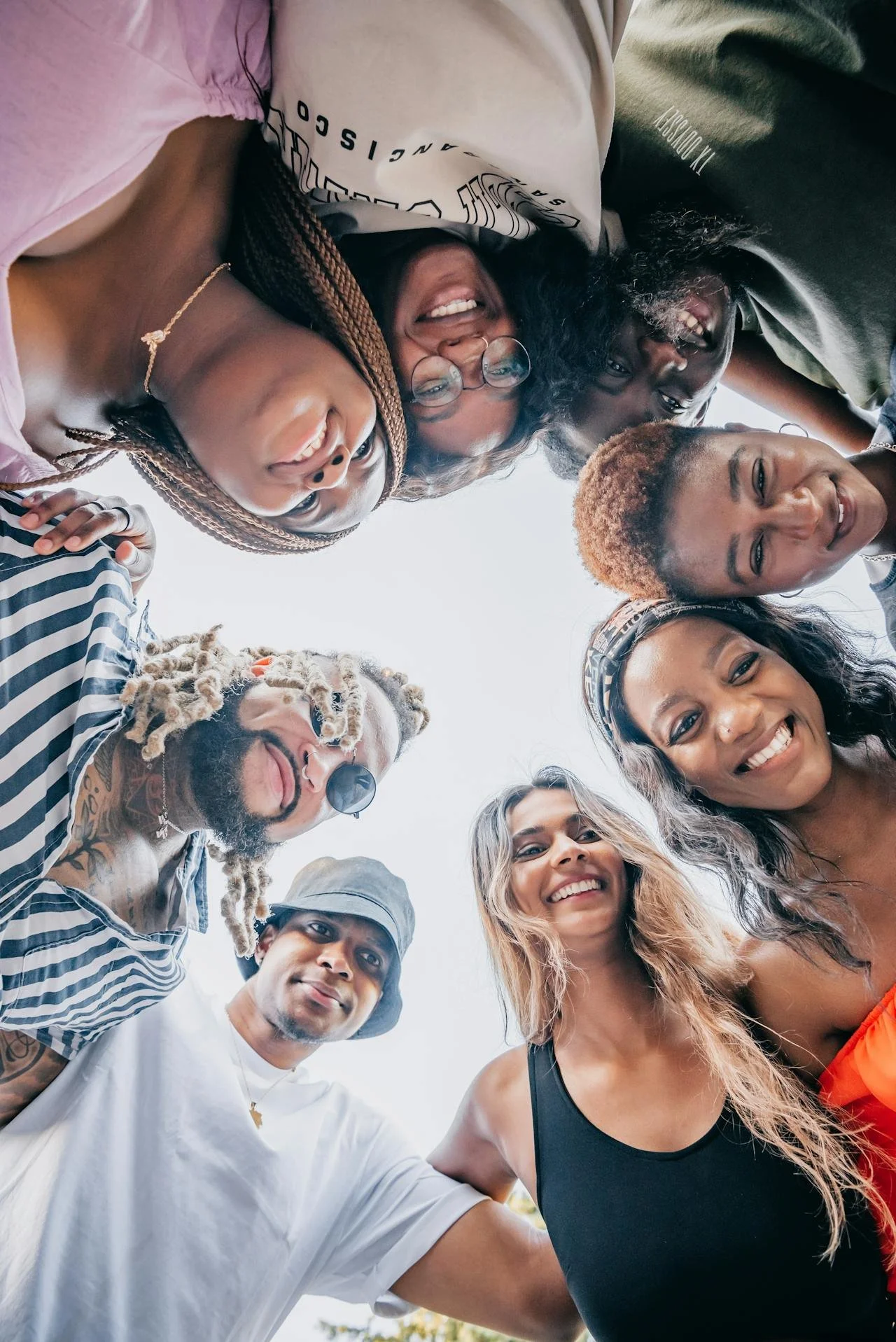 Diverse group of adults standing in a circle looking down at the camera and smiling