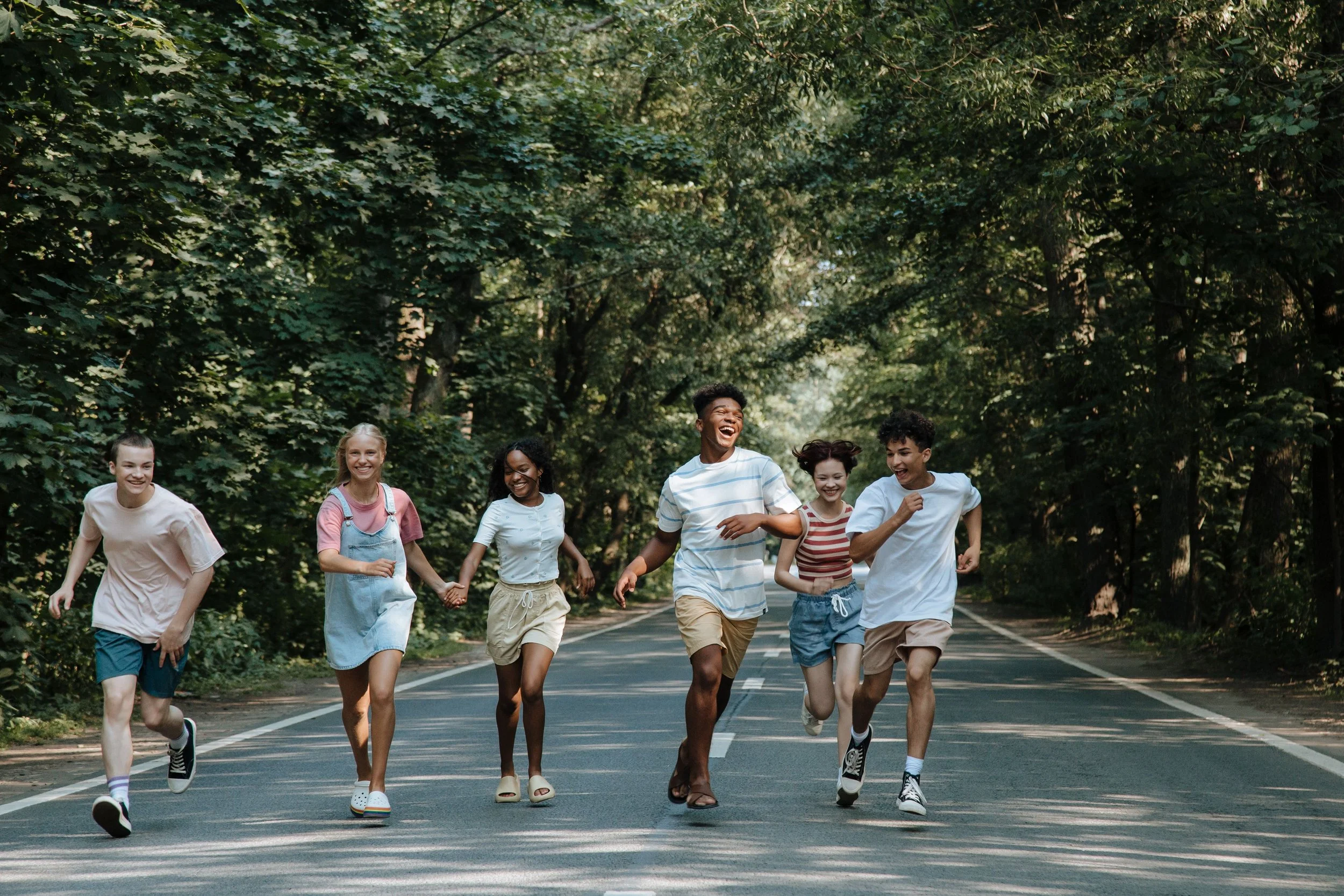 Group of diverse young people running together outdoors on a tree-lined path