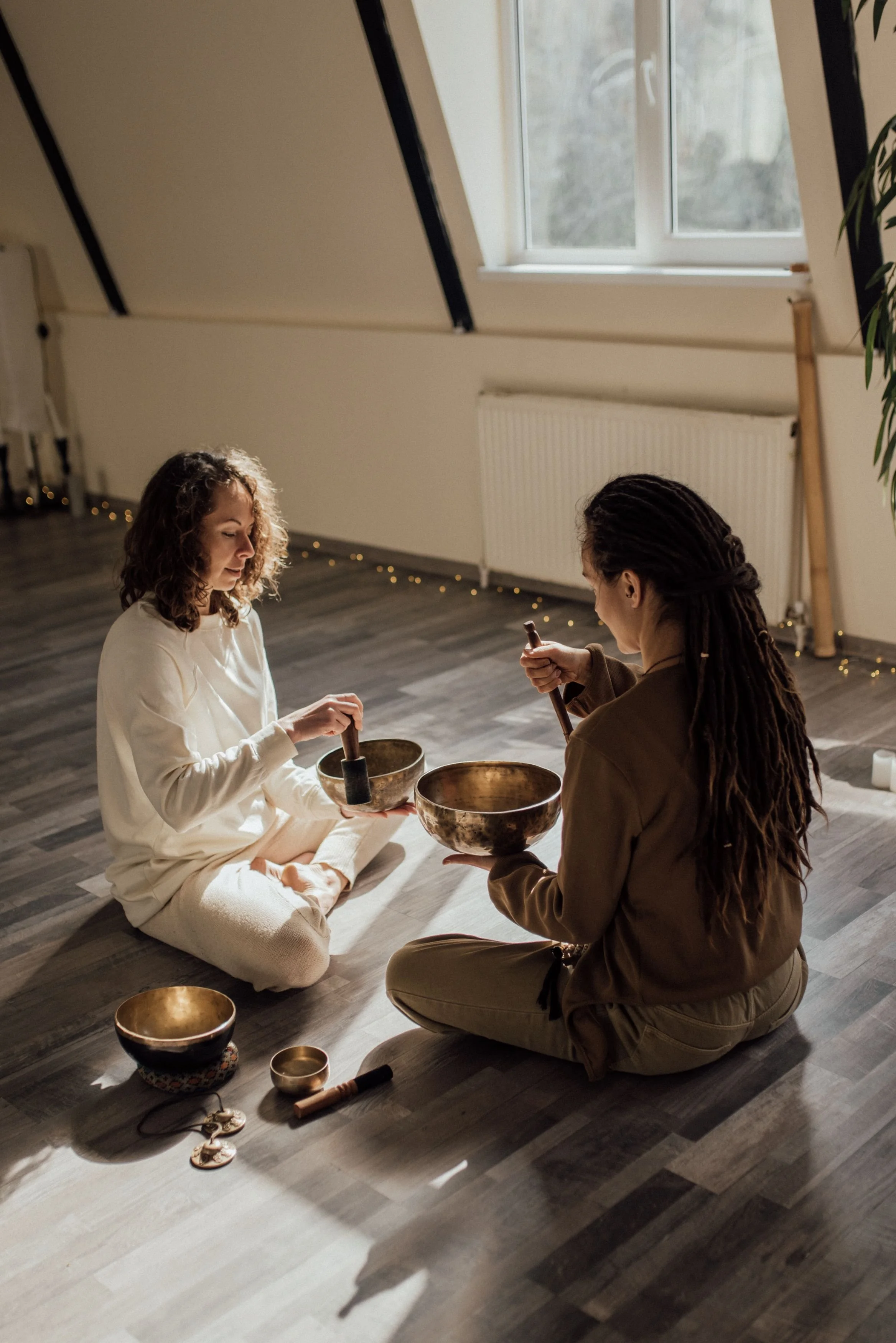 Two women sitting on the floor holding brass singing bowls during a sound healing session