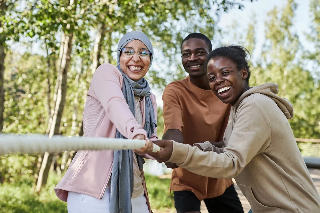 Three young people smiling and pulling a rope together during an outdoor team activity