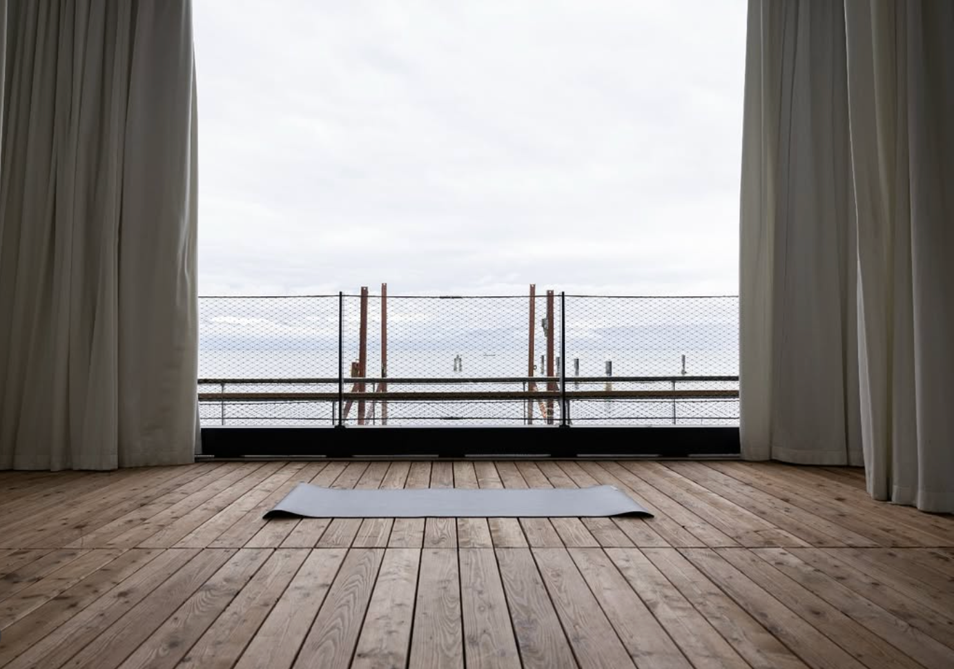 Leerer Raum mit Holzfußboden und großen Fenstern, die einen Blick auf den Bodensee im Freien bieten.