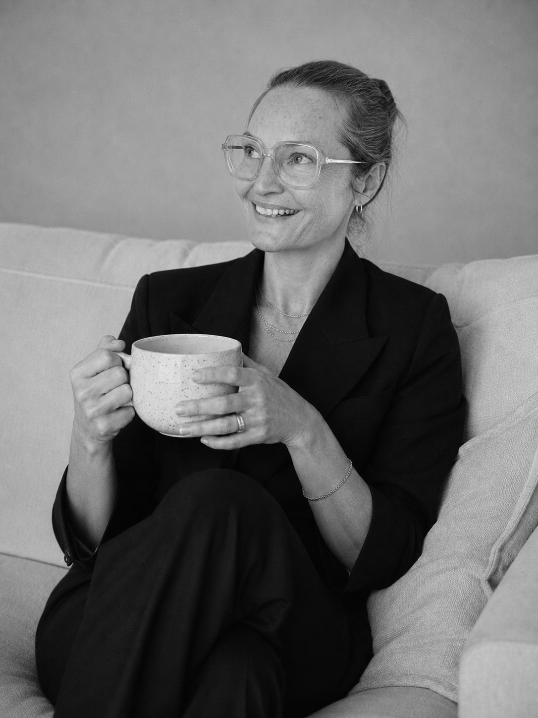 Nerina, sober life coach, alcohol-free since 2018, smiling sitting on a sofa with a big mug of tea..