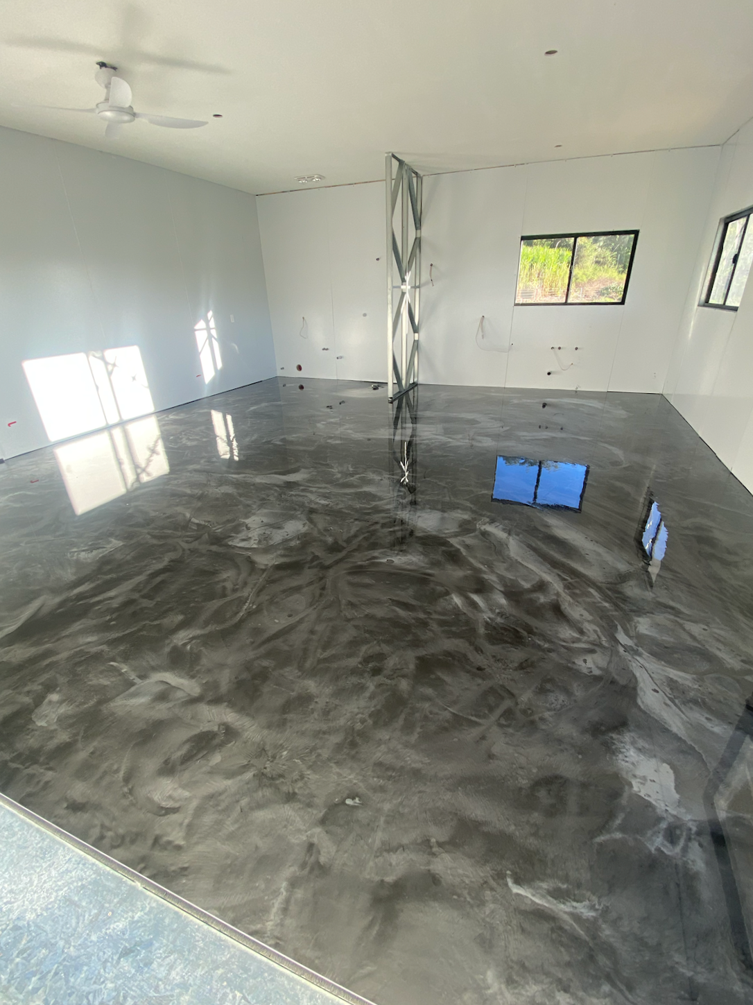 Interior view of an unfinished room with shiny concrete floor, white walls, windows, and a ceiling fan.