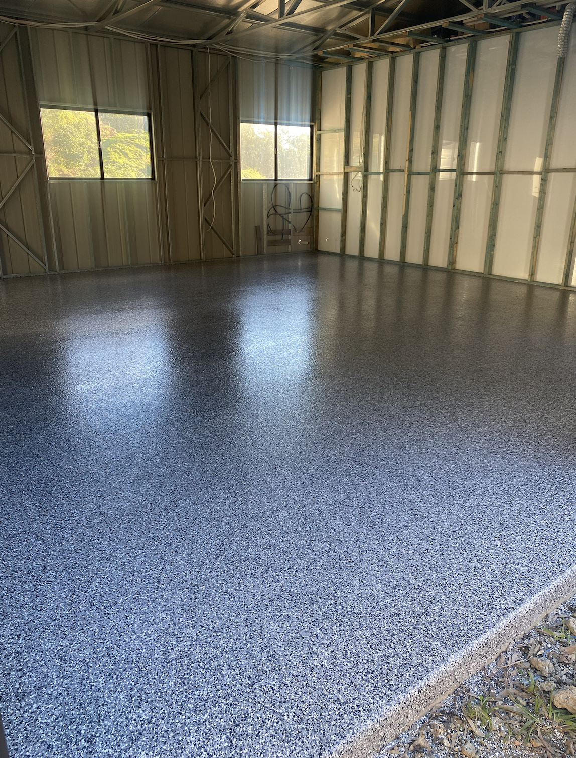 Unfinished interior of a building with metal framing and two windows, showing a newly poured textured concrete floor.