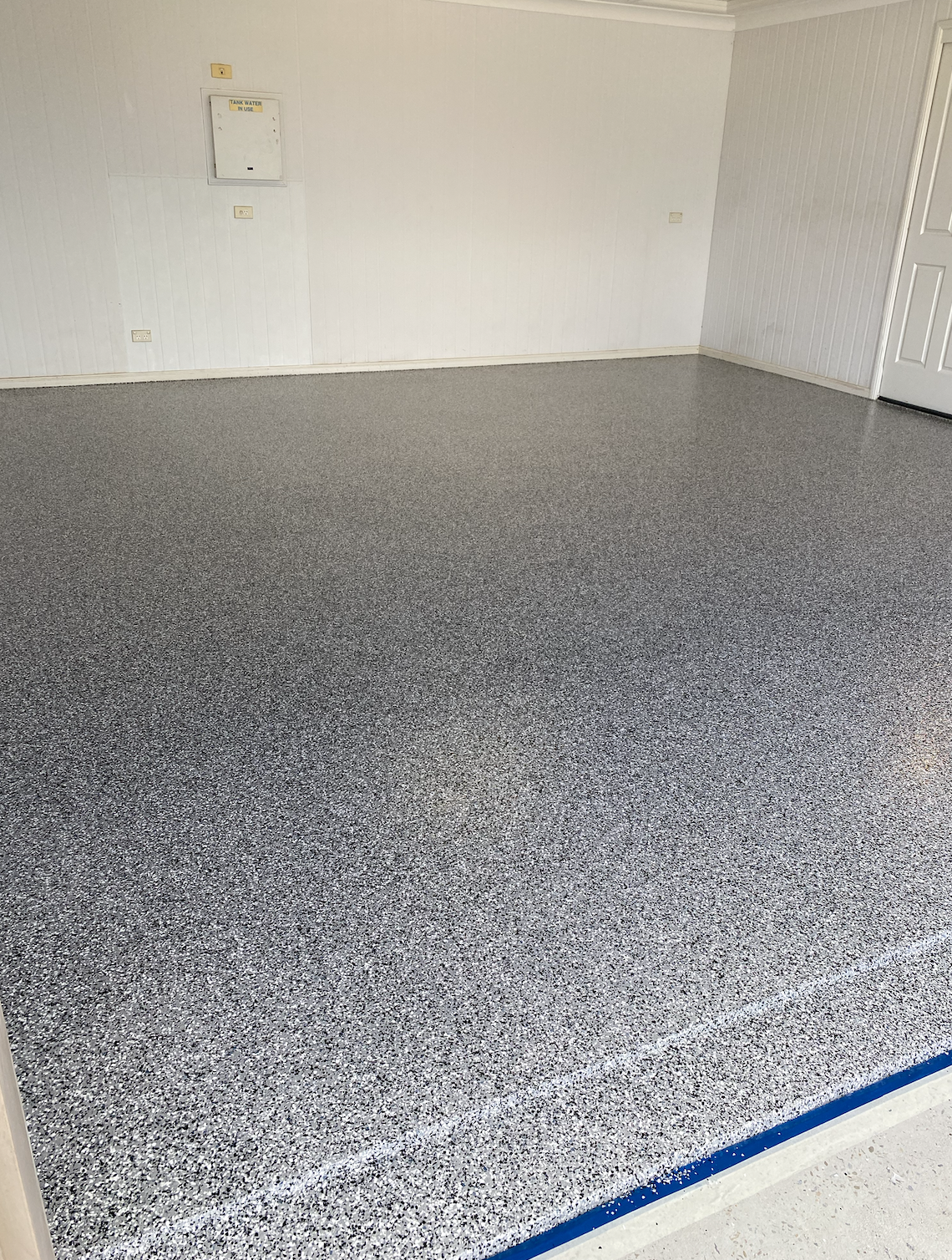 Empty room with white walls, gray speckled epoxy flooring, and some electrical panels on the wall.