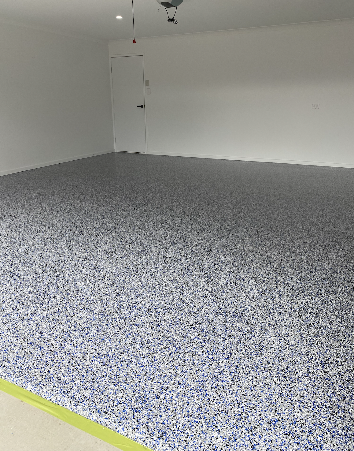 Empty room with speckled gray and white flooring, white walls, and a ceiling light fixture hanging from the ceiling.