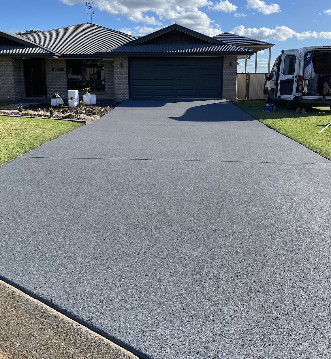 Newly poured smooth concrete driveway leading to a garage attached to a brick house under a partly cloudy sky.