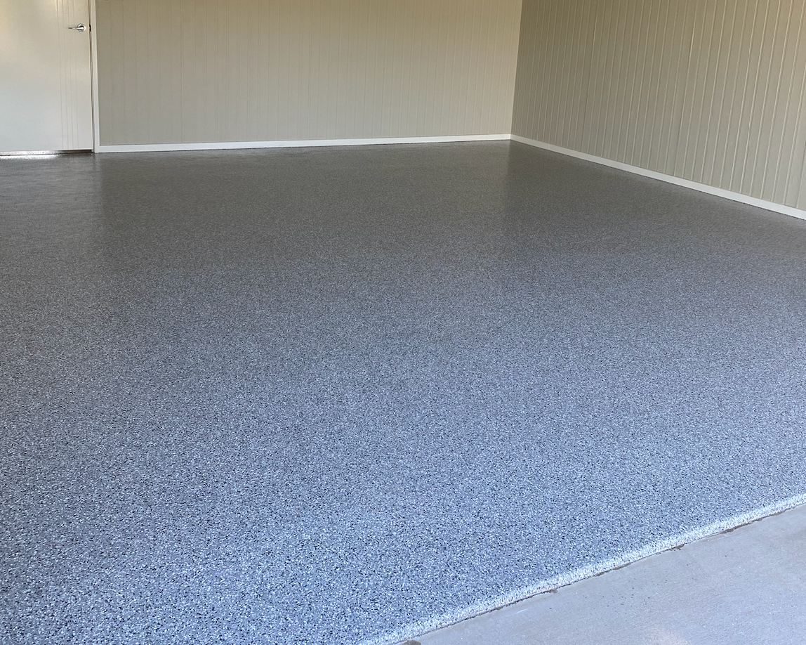 Empty room with gray speckled epoxy flooring and beige paneled walls.