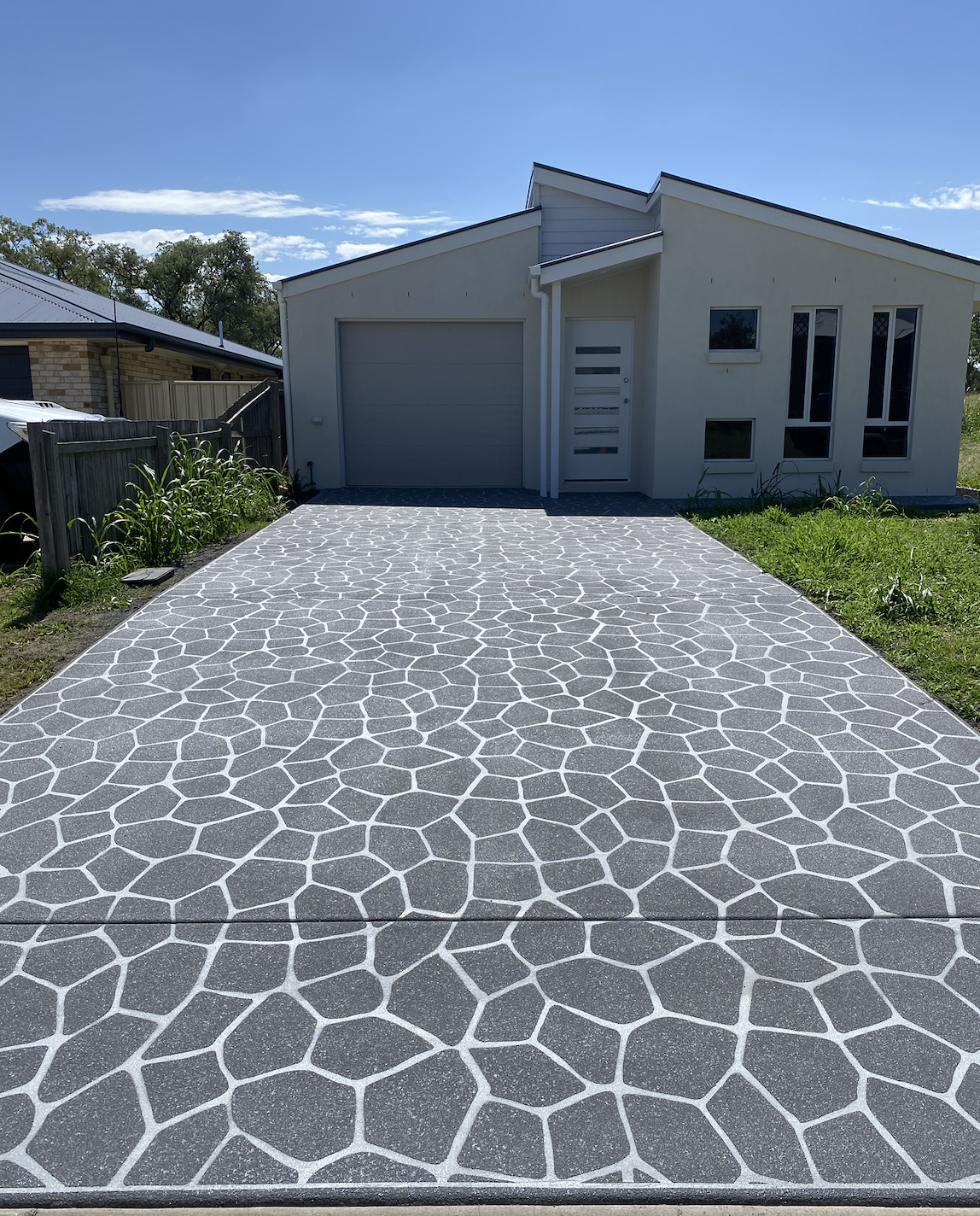 Modern house with a patterned concrete driveway, white exterior walls, and several narrow windows under a blue sky.