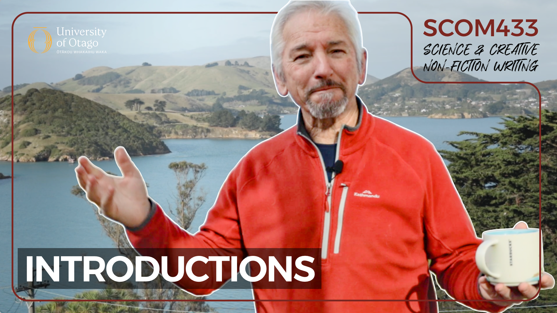 A man with gray hair and a beard wearing a red jacket, standing outdoors with a scenic view of a lake and rolling hills in the background, holding a coffee mug and gesturing with his right hand, appears to be speaking or explaining.