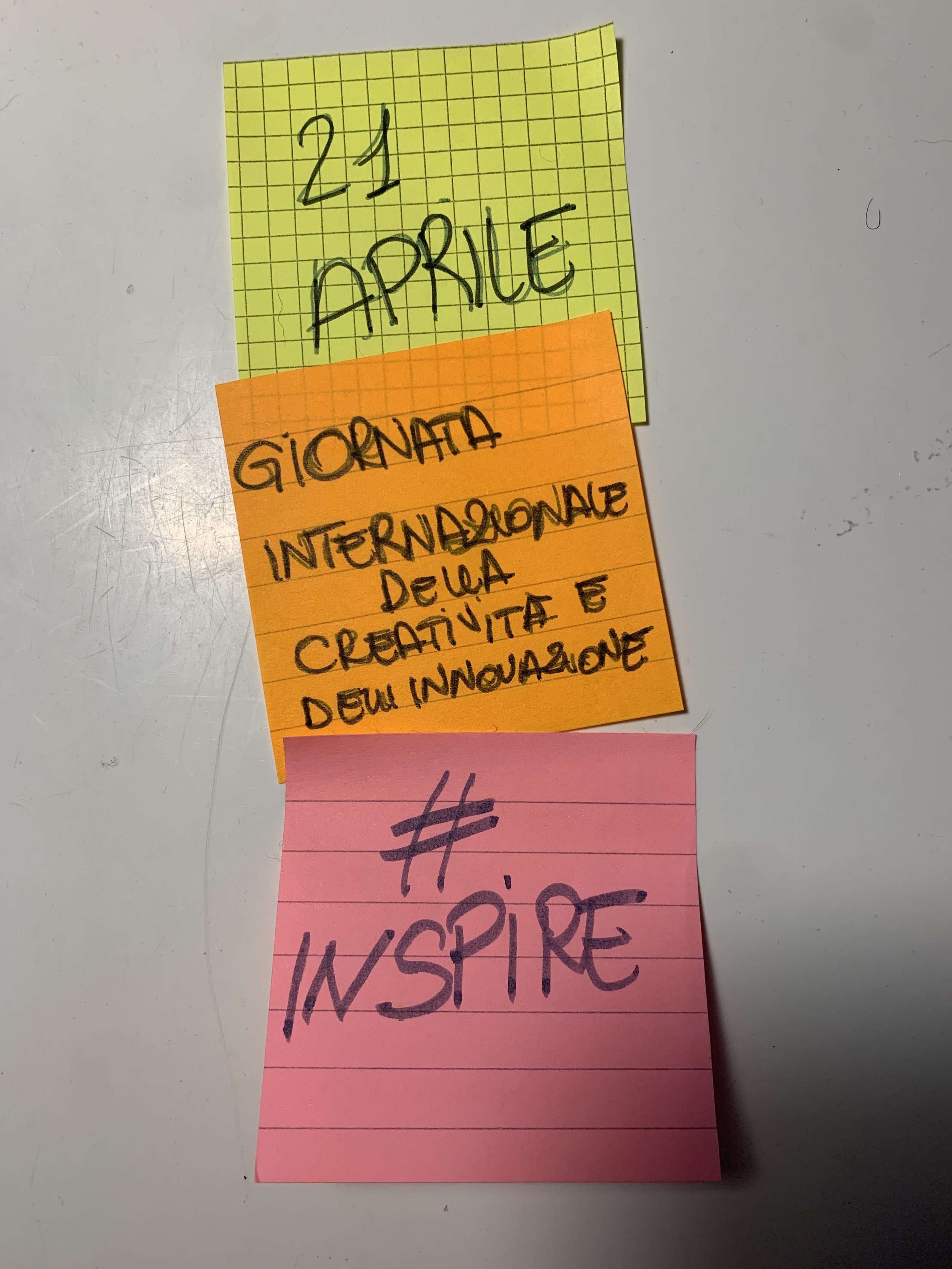 Tre note adesive con testo: "21 Aprile" su foglio giallo, "Giornata Internazionale della Creatività e dell'Innovazione" su foglio arancione, e "#Inspire" su foglio rosa.
