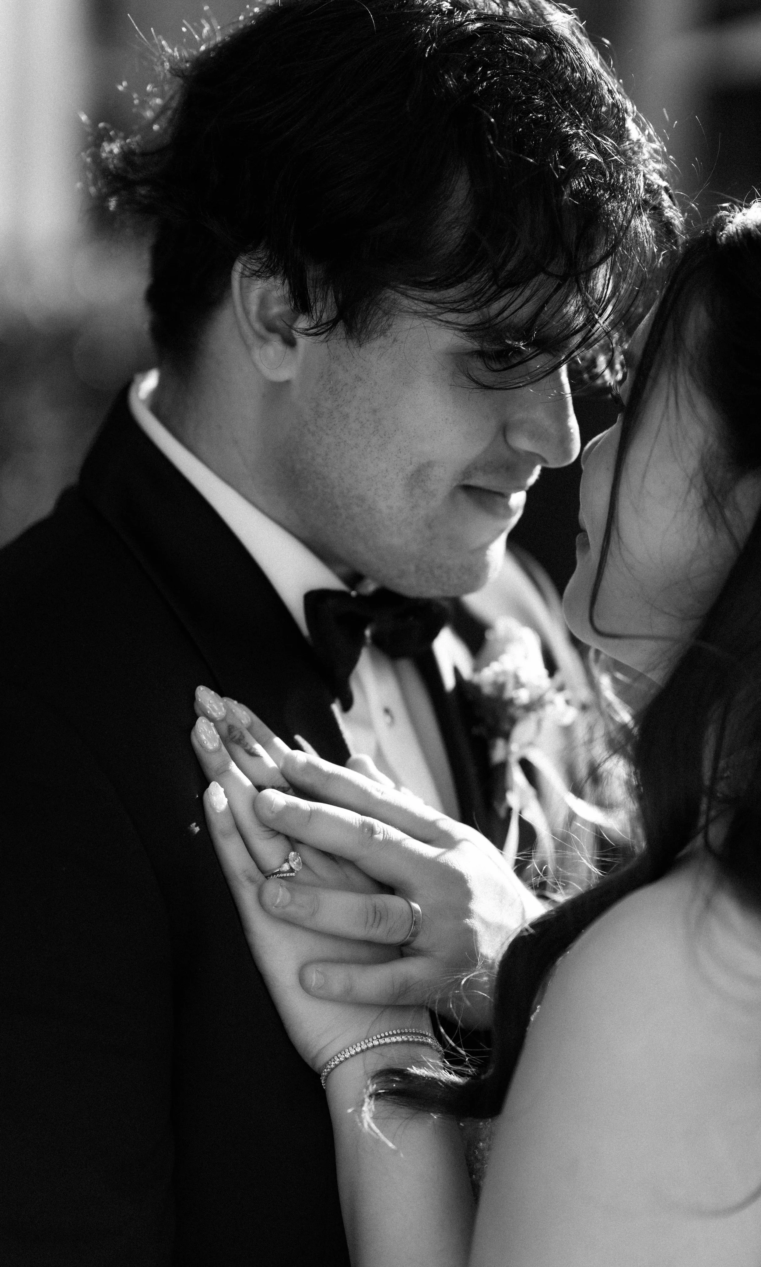 Black and white photo of a couple dancing closely, holding each other's hands, smiling with their faces close together, during a wedding.