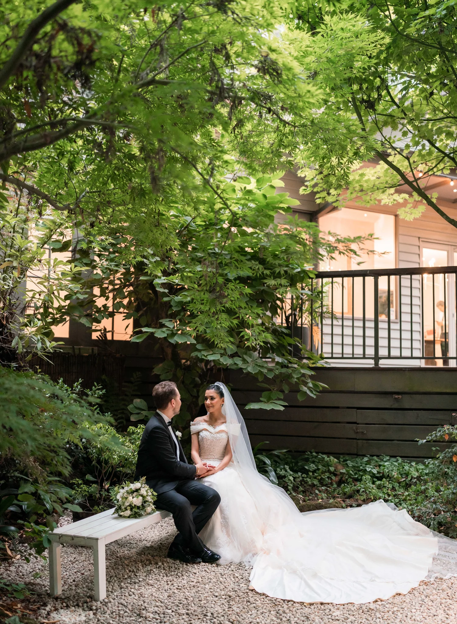 A bride and groom sitting together in a garden, sharing a quiet moment on their wedding day.