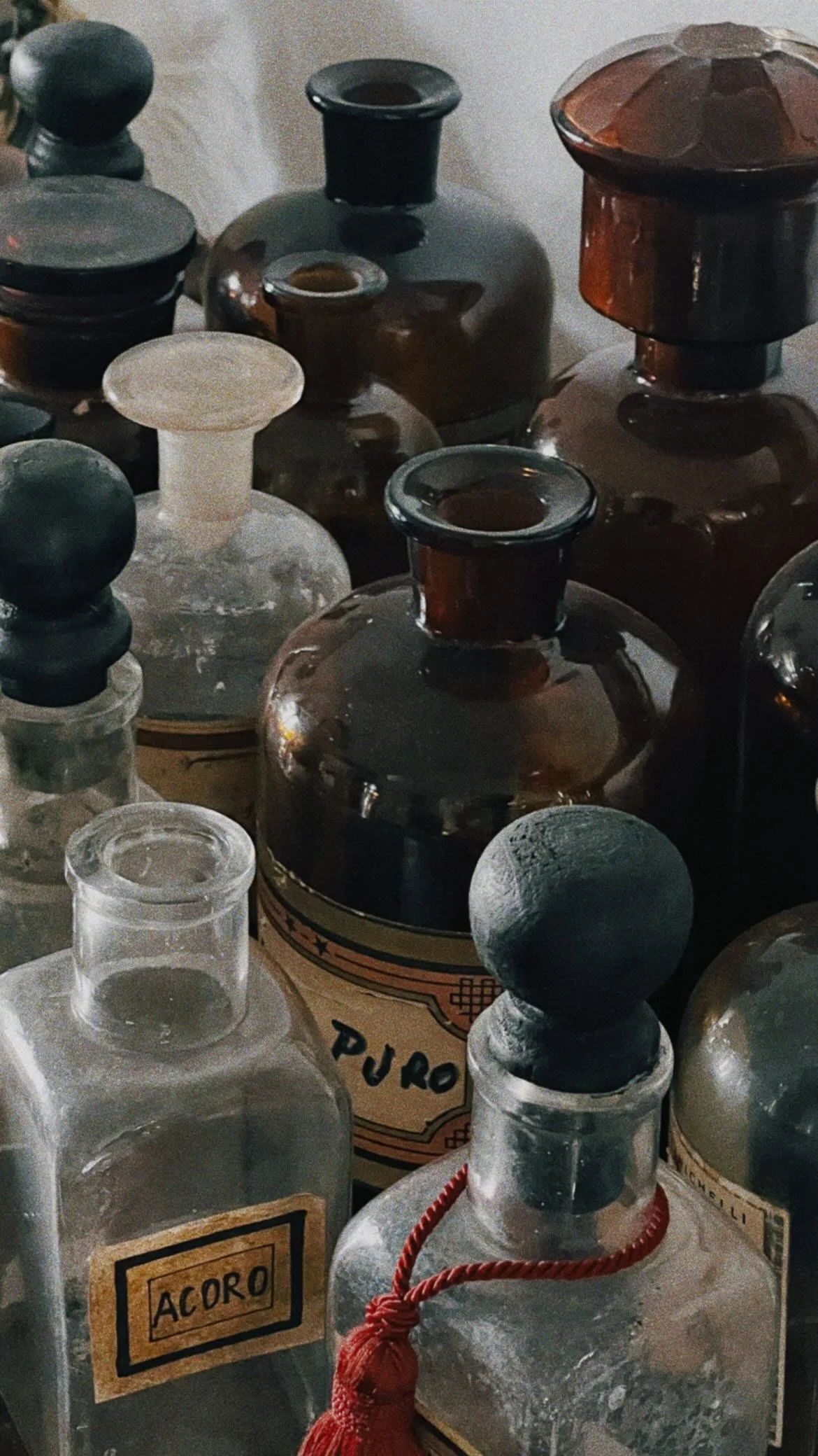 A collection of vintage glass bottles, some with cork stoppers, with labels that read 'ACORO' and 'PURO', on a cluttered surface.
