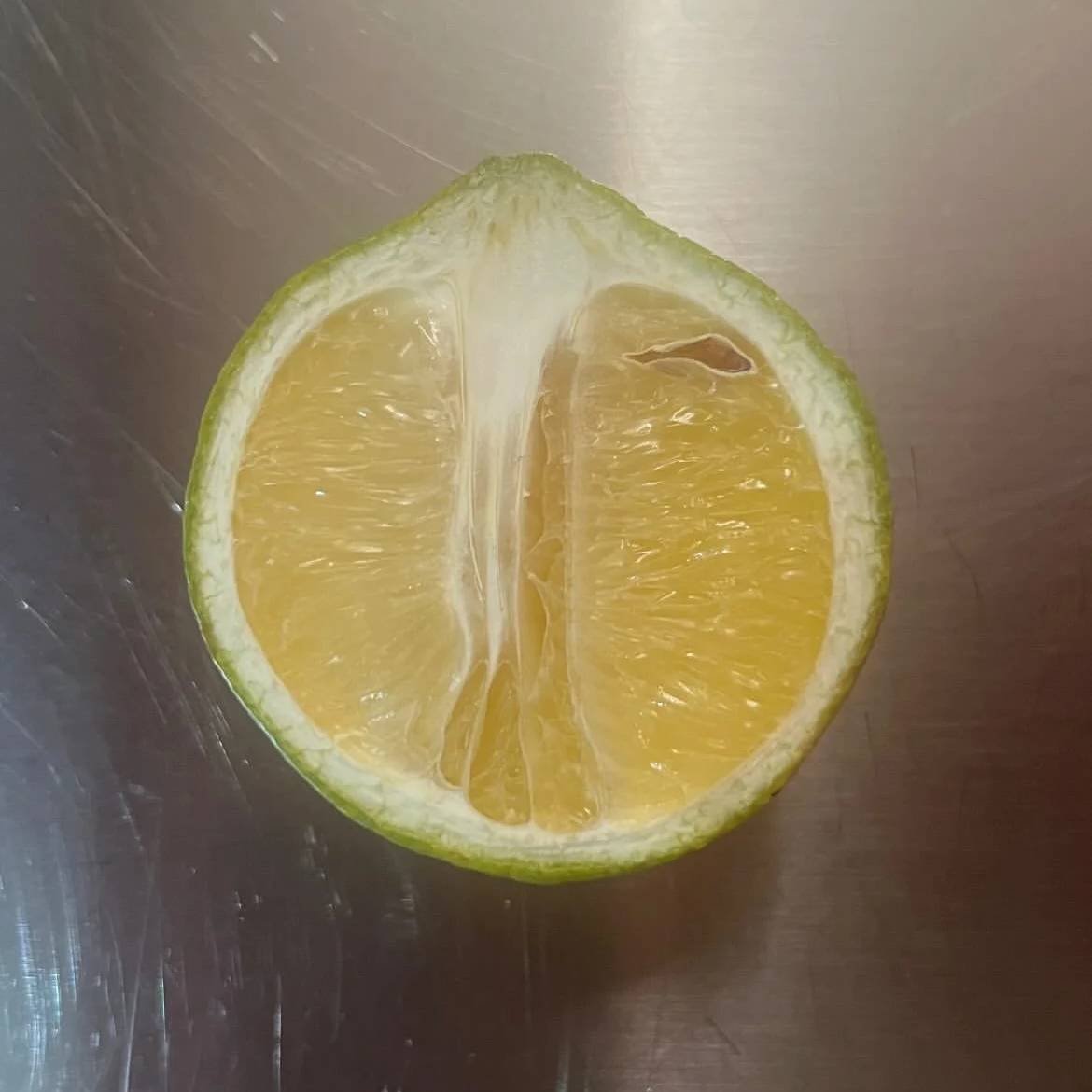 Half a lemon with yellow flesh on a metallic surface.