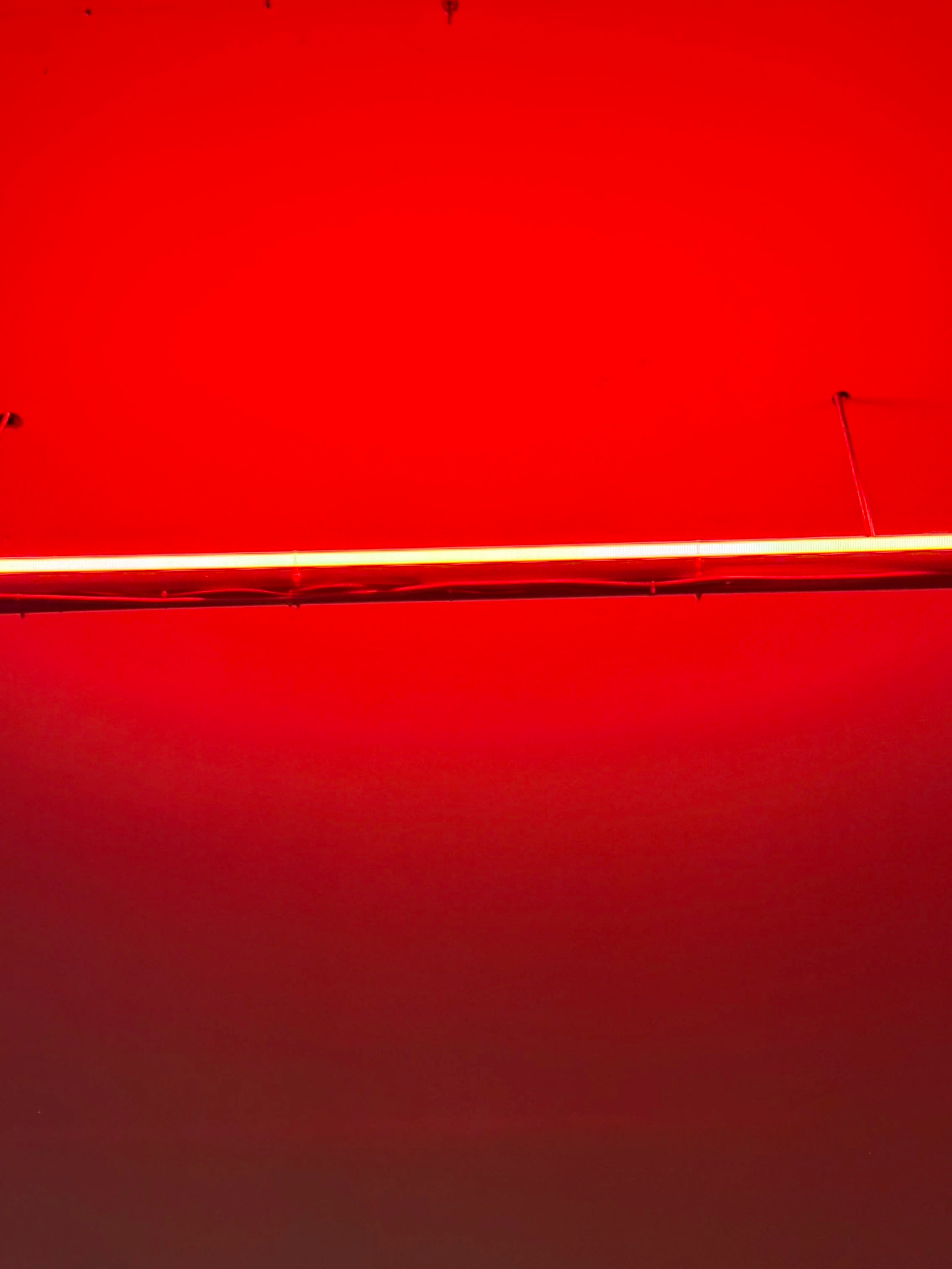 A red wall with a horizontal illuminated neon light strip running across the middle.