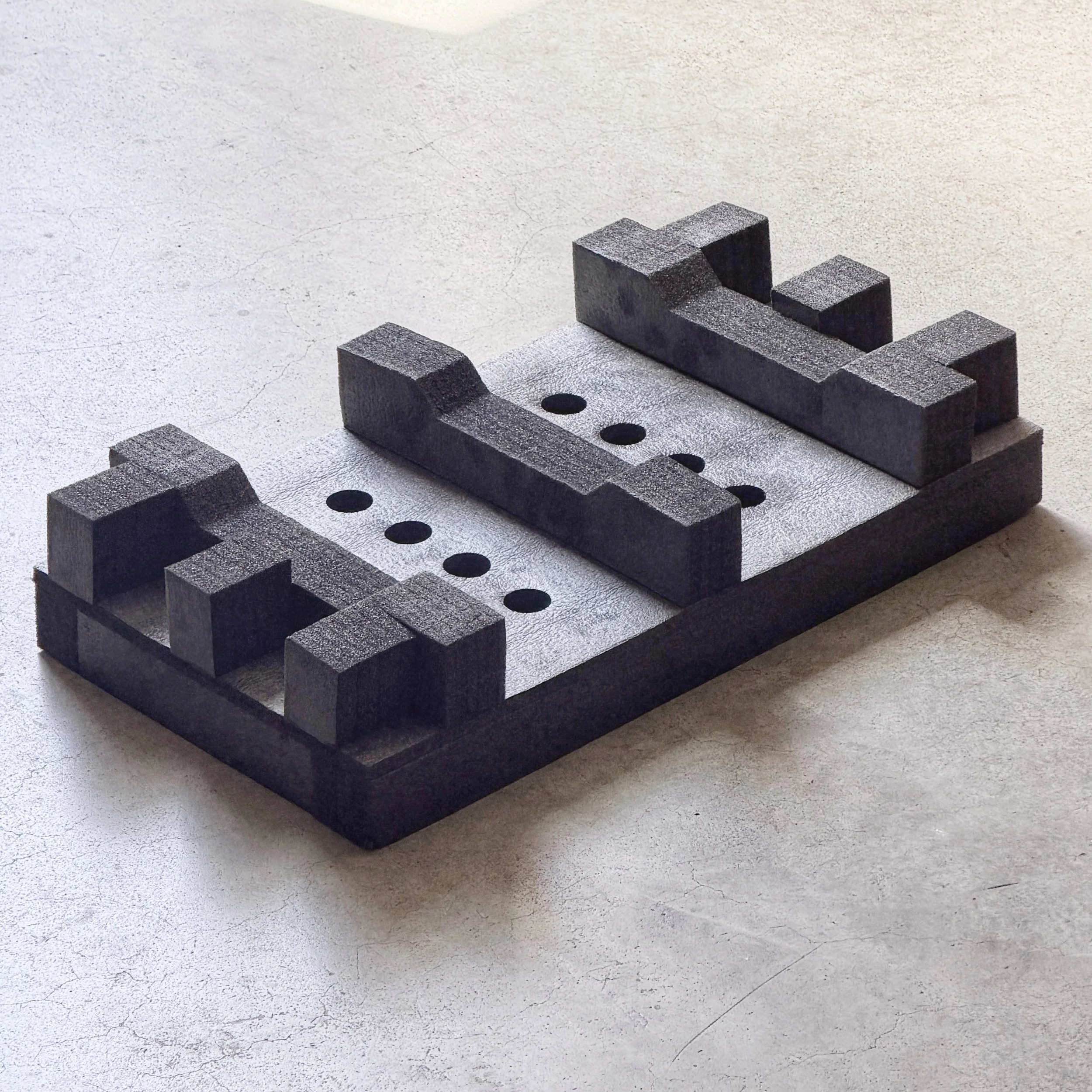 Close-up of small black wooden blocks stacked on top of a larger black wooden base on a textured light-colored surface.