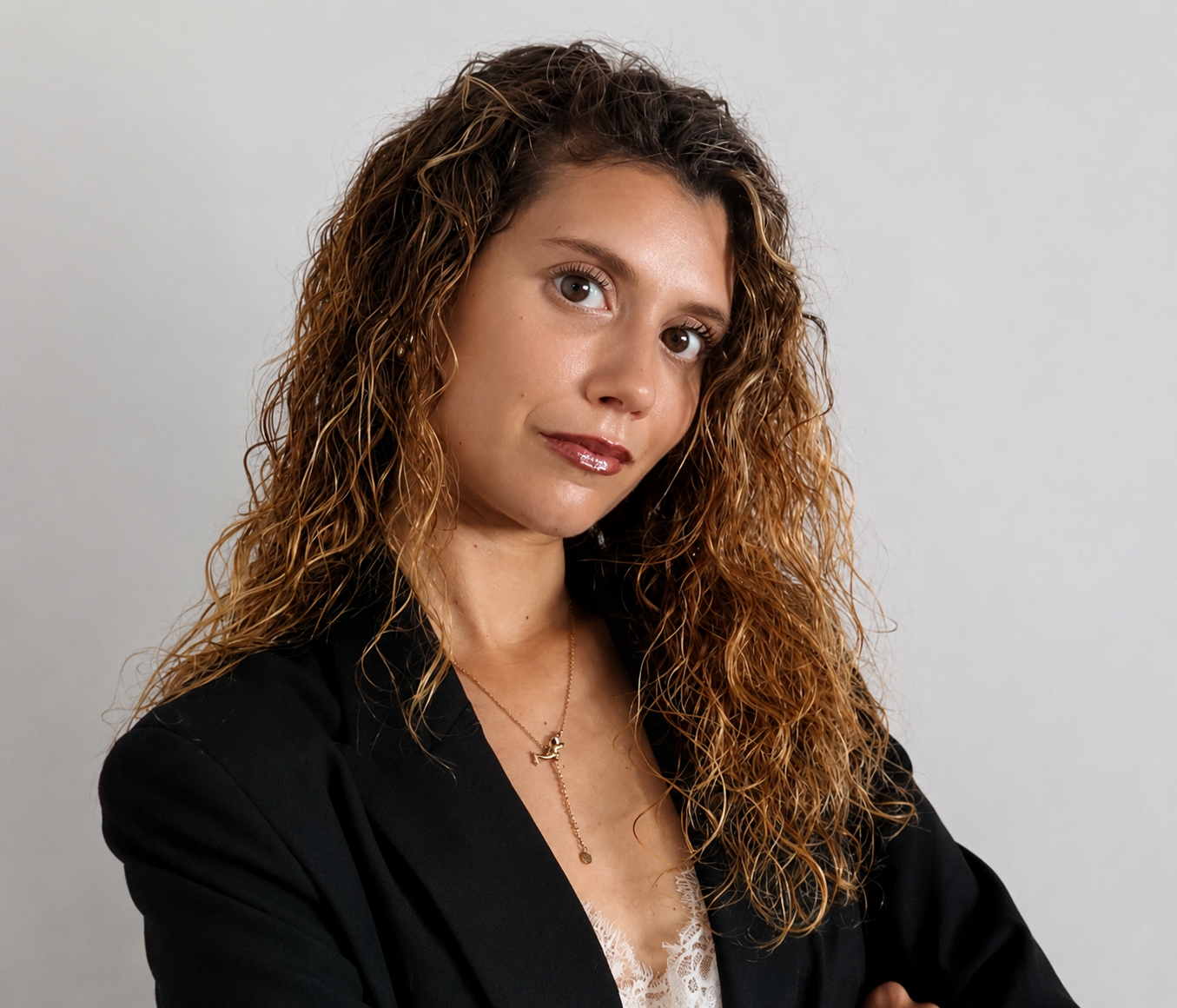 Retrato de una mujer con cabello rizado y castaño aclarado, vestida con blusa blanca y abrigo negro, sonriendo ligeramente, con fondo gris claro.