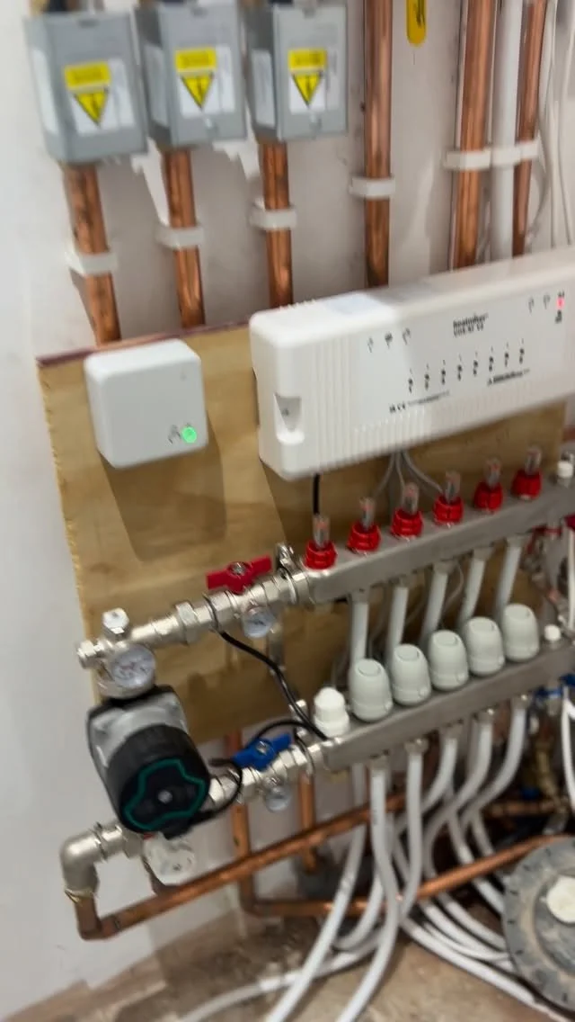 Electrical and plumbing components mounted on a wall, including circuit breakers, a control panel, pipes, and valves.