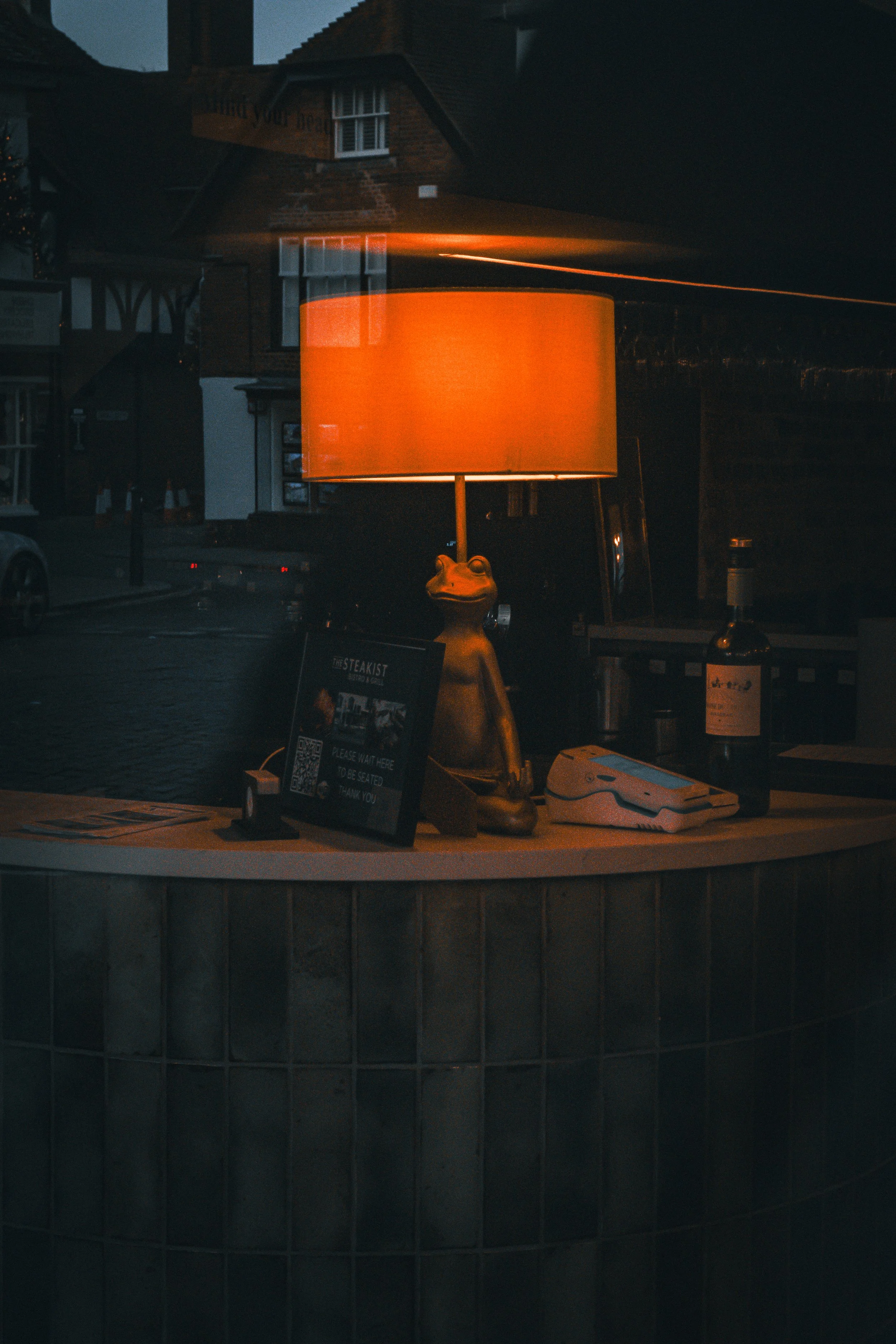 A frog statue holding a large orange illuminated sign in front of buildings at night.