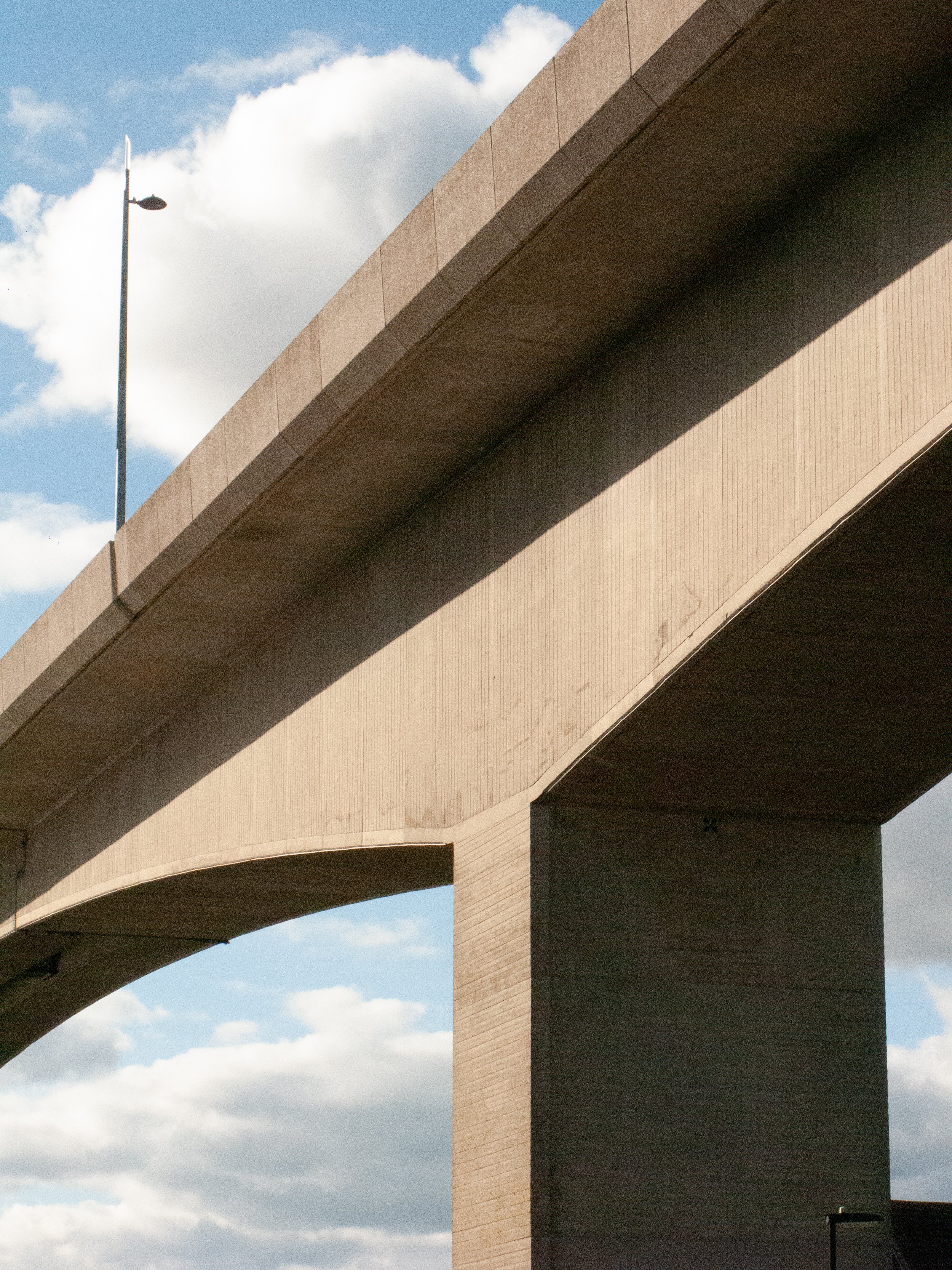 Close-up view of a large concrete bridge with a segment of the roadway and support columns against a partly cloudy sky.