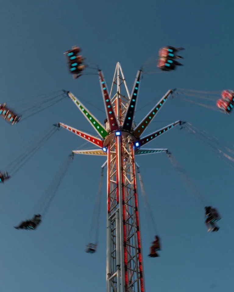 A tall amusement park swing ride with swings spinning against a clear blue evening sky.