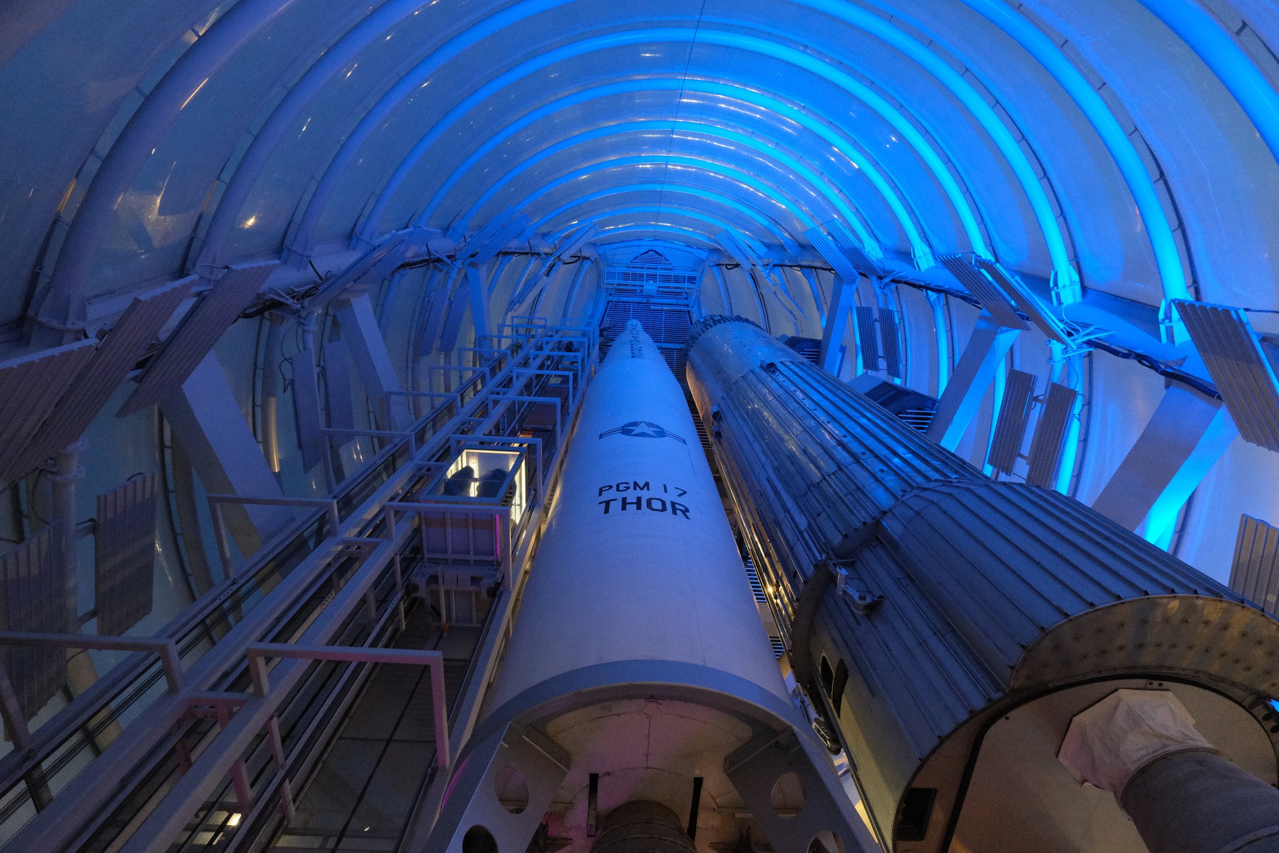 Inside view of a space launch pad with a rocket labeled 'PGM-17 Thor' and blue lighting illuminating the curved architecture.
