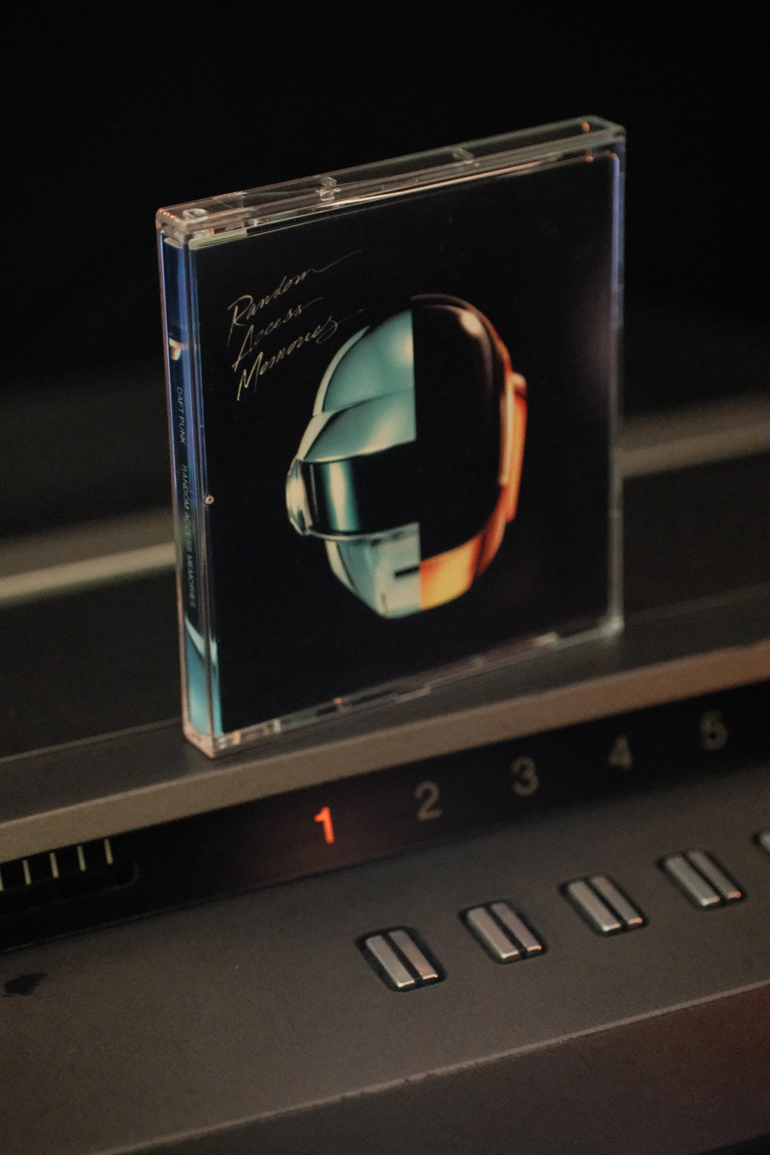 A cassette tape case with artwork of a futuristic helmet and the phrase 'Runaway, Endless, Morrows' on a dark background, placed on an electronic device or instrument.