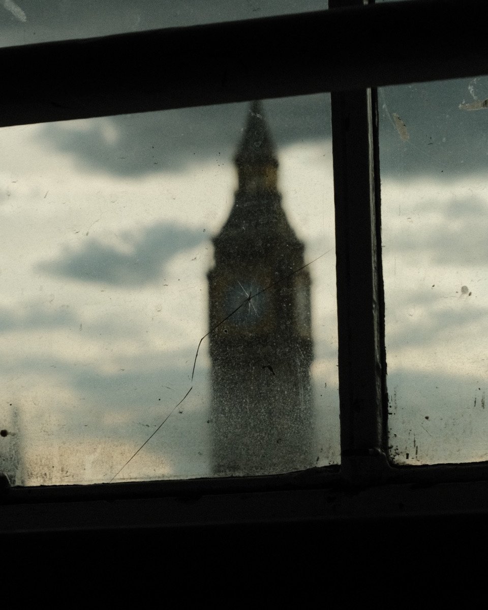 View of Big Ben through a dirty window with cracks, surrounded by clouds.