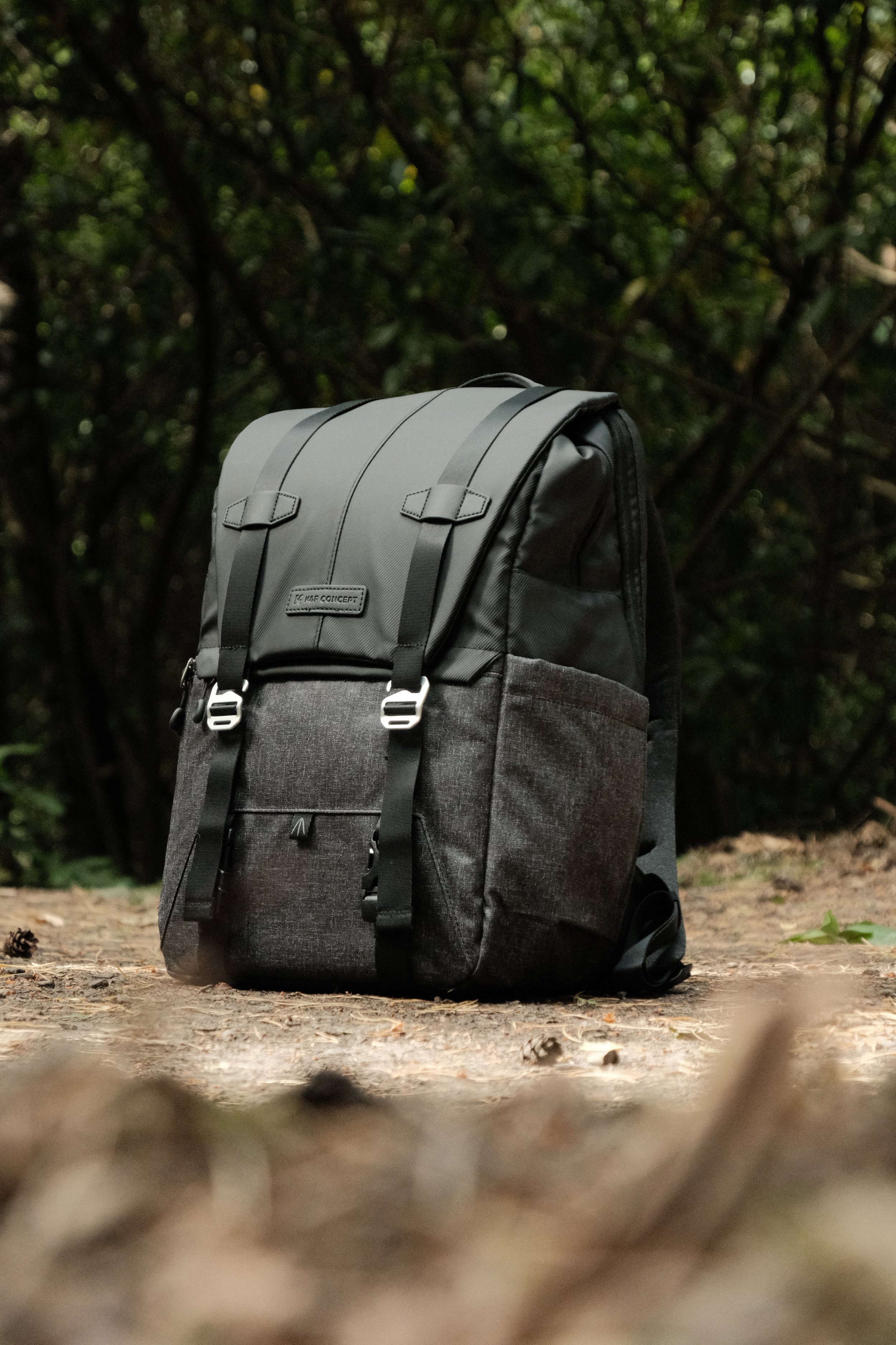 A gray and black backpack placed on the ground in a wooded outdoor setting.