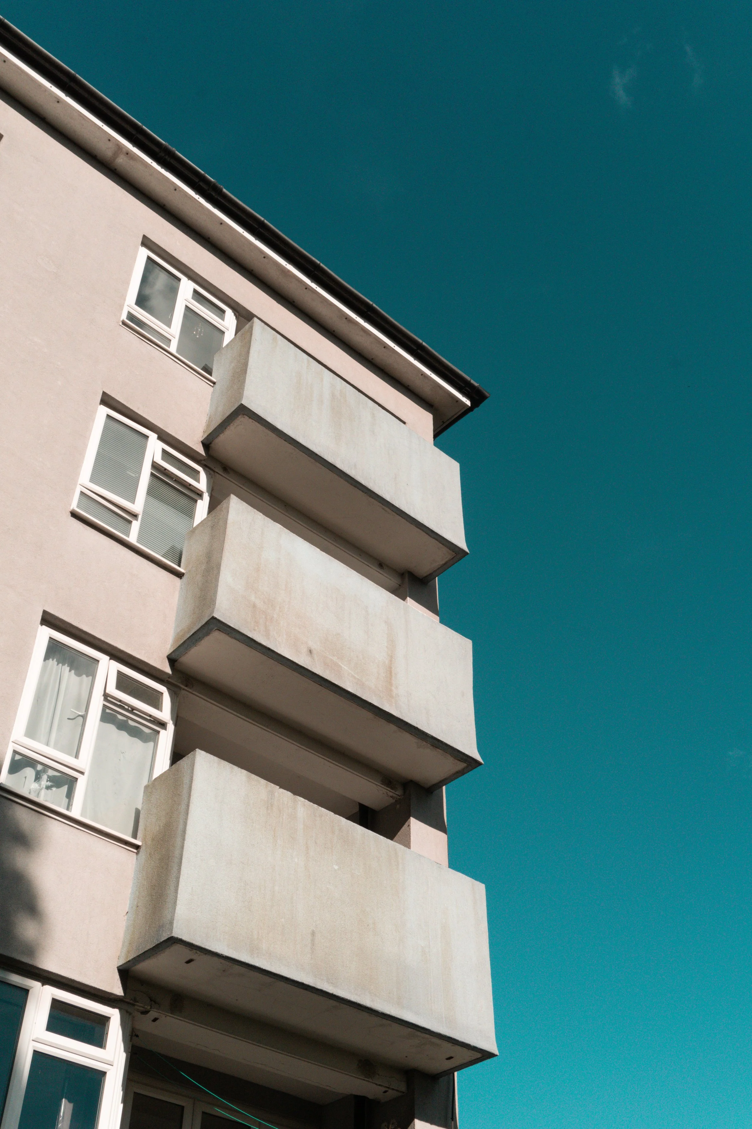 A beige multi-story building with many balconies and windows against a clear blue sky.