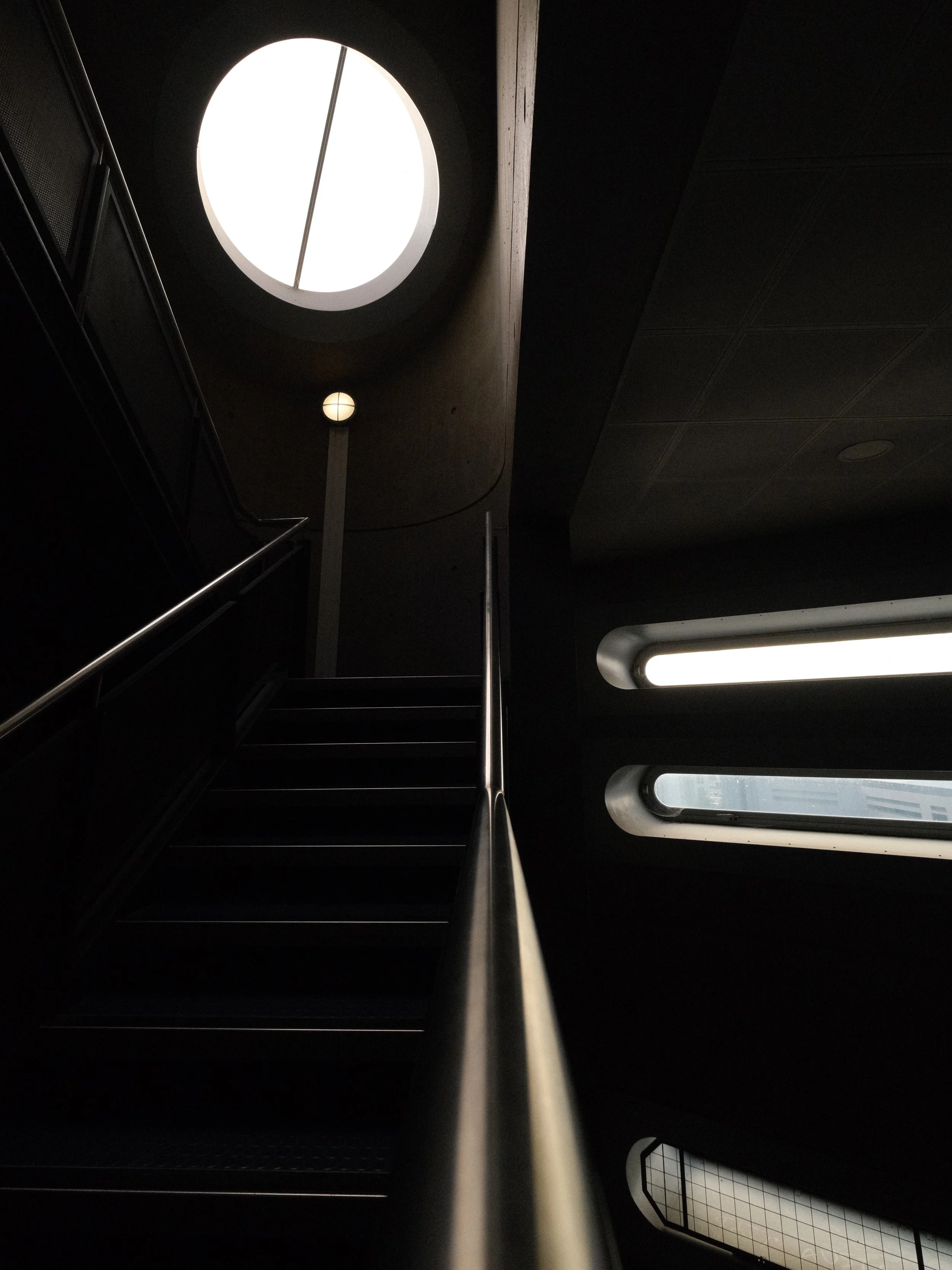 Interior view of a modern building with a staircase, circular skylight, and windows with rounded edges.