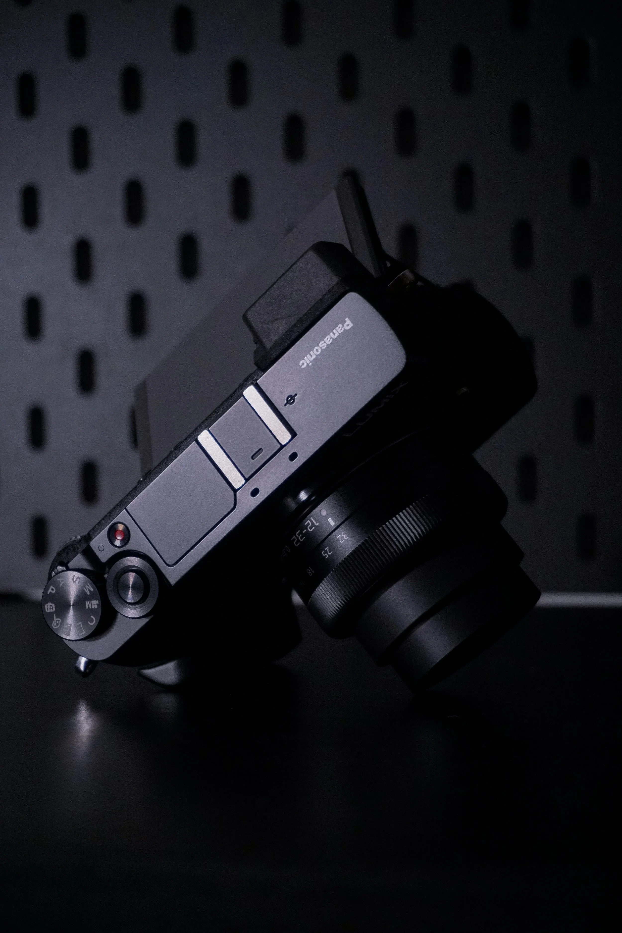 A Panasonic digital camera with a zoom lens attached, resting against a black, perforated background.