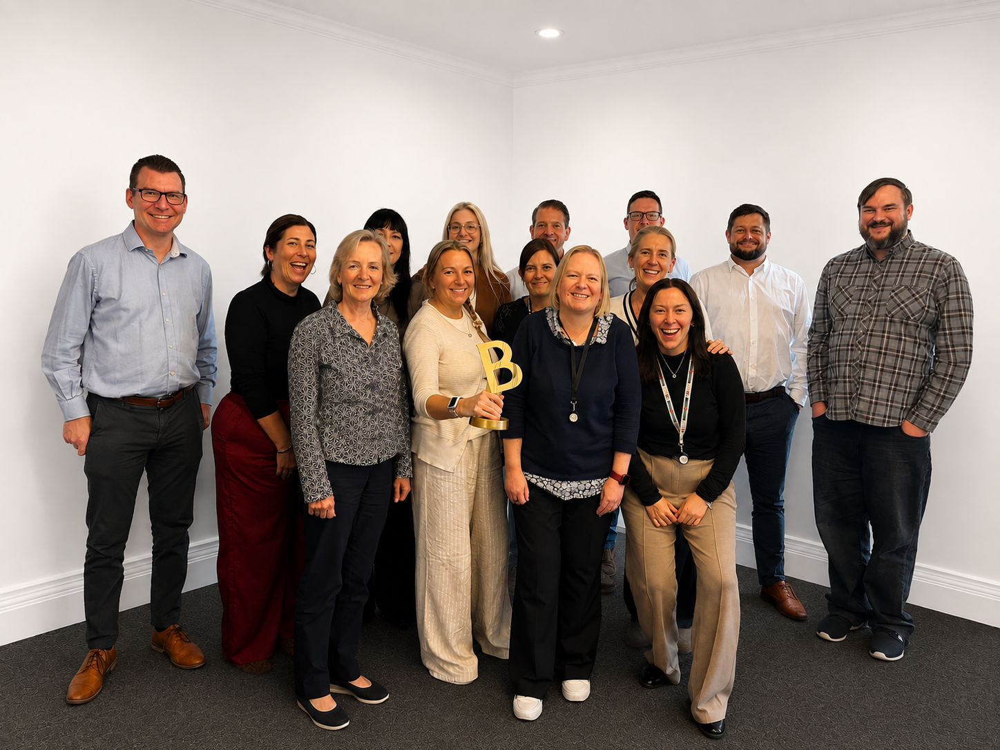 Group of 13 professionals standing in an office corner, smiling, with one woman holding a gold award shaped like the letter B.