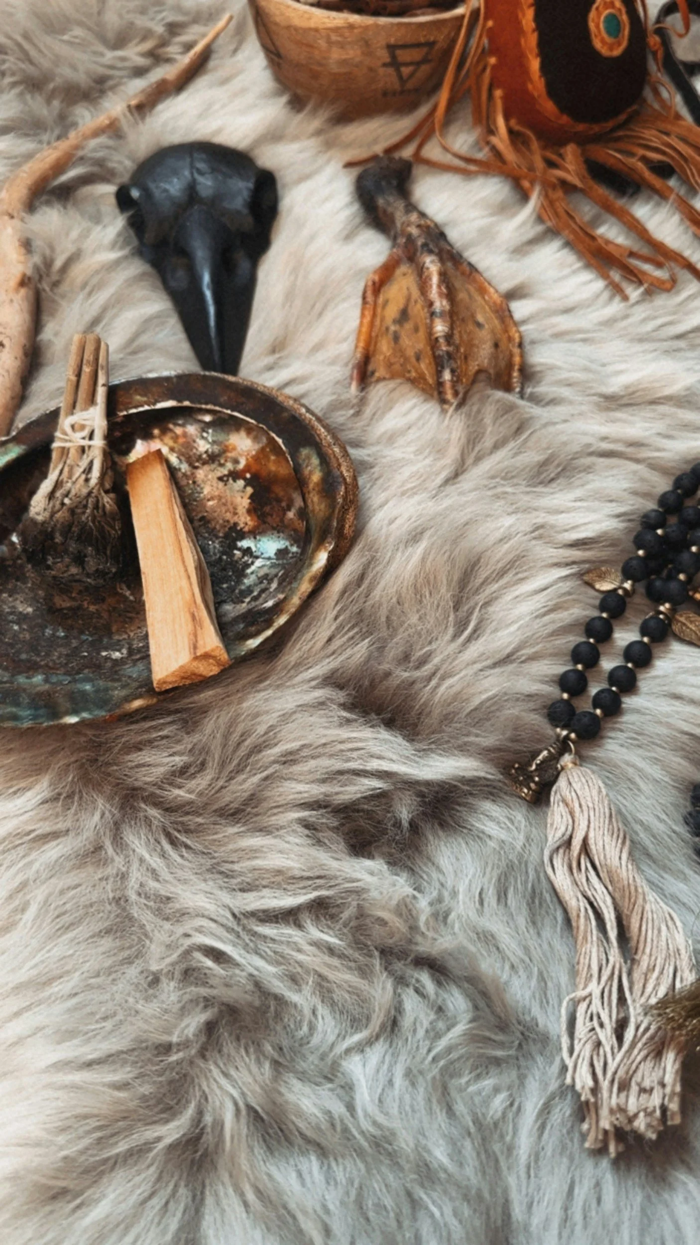 A black bird skull, wooden objects, a beaded necklace, a leather and fabric decorative item, and a fluffy white fur background.
