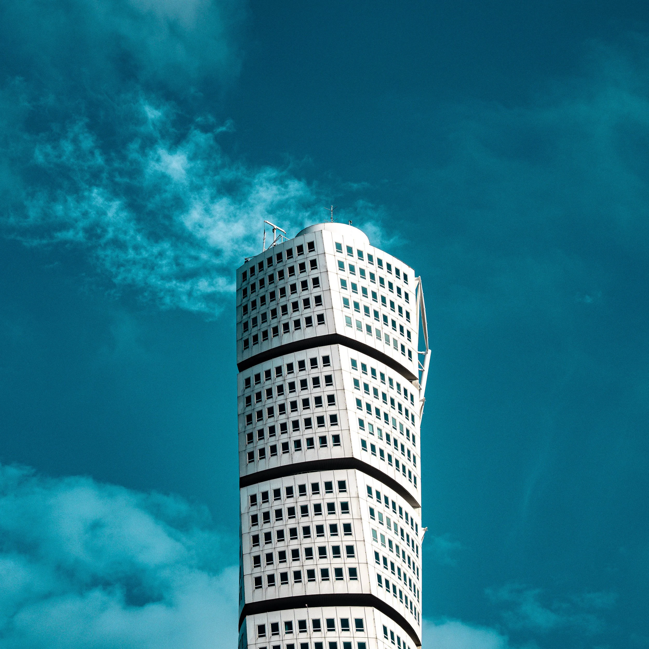 The Turning Torso, a white skyscraper in Malmö, Sweden with a unique curved design and numerous windows, set against a blue sky with some clouds.