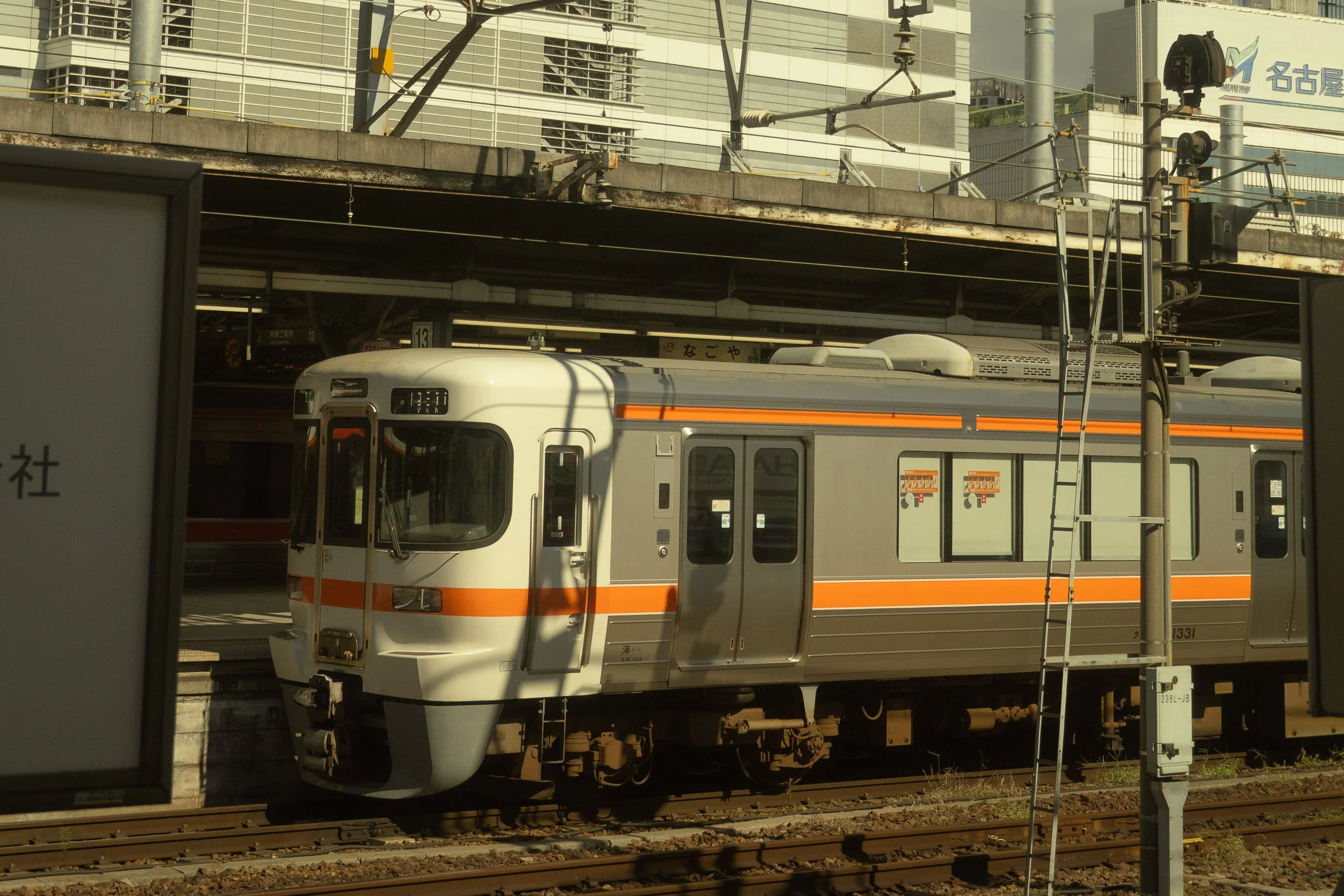A train station with a train on the tracks in Japan, overhead electrical wires, and a modern building in the background.